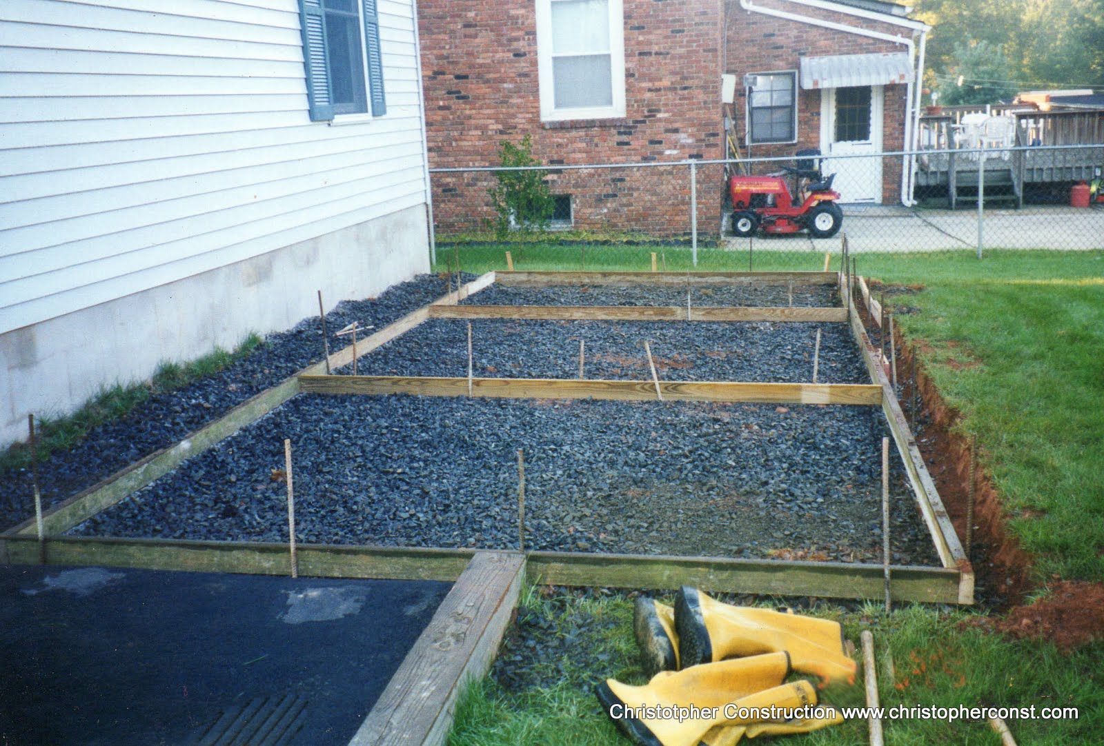 Backyard garden beds framed with wood beside a house, filled with dark soil and gravel pathways
