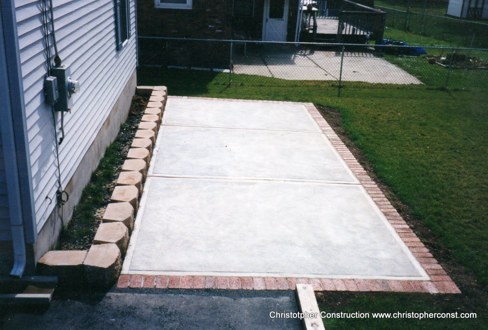 Concrete patio beside house with brick border and landscaped yard