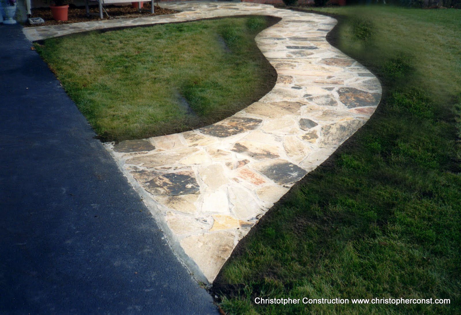 Curved stone walkway bordered by grass beside a dark asphalt path.