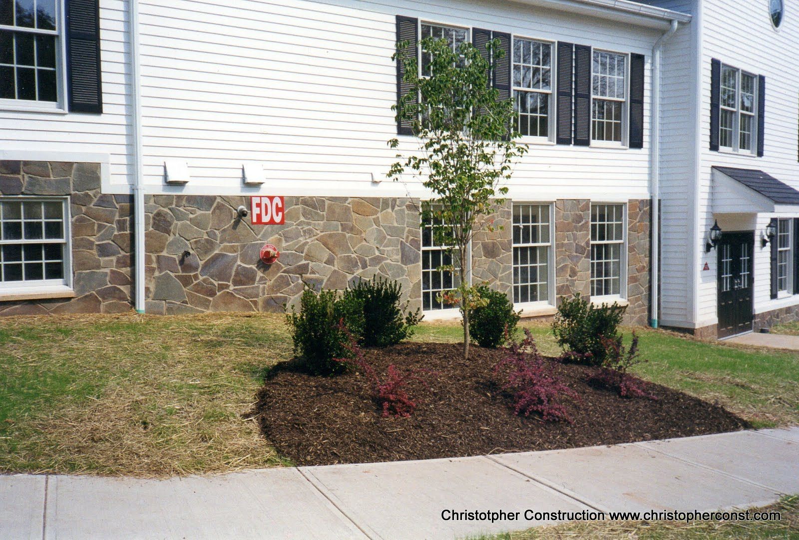 White townhouse exterior with stone facade, sidewalk, and landscaped shrubs near unit 106