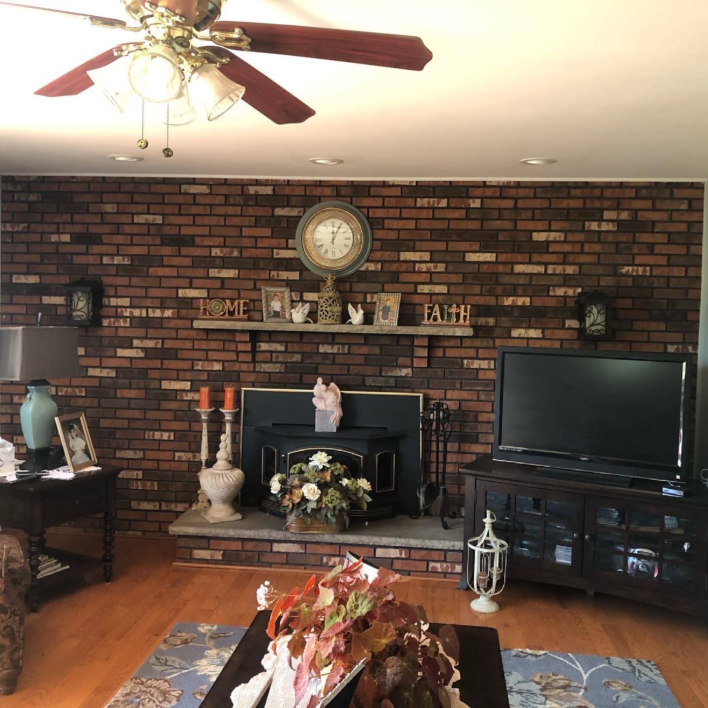 Cozy living room with brick fireplace, TV, ceiling fan, hardwood floor, and floral arrangement on a table.