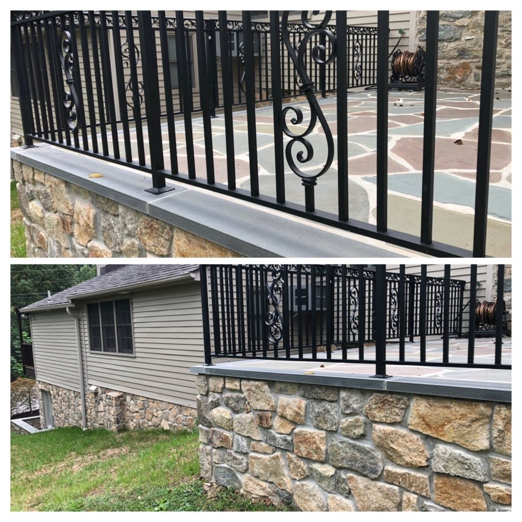 Black metal railing atop a stone retaining wall beside a house and patio.