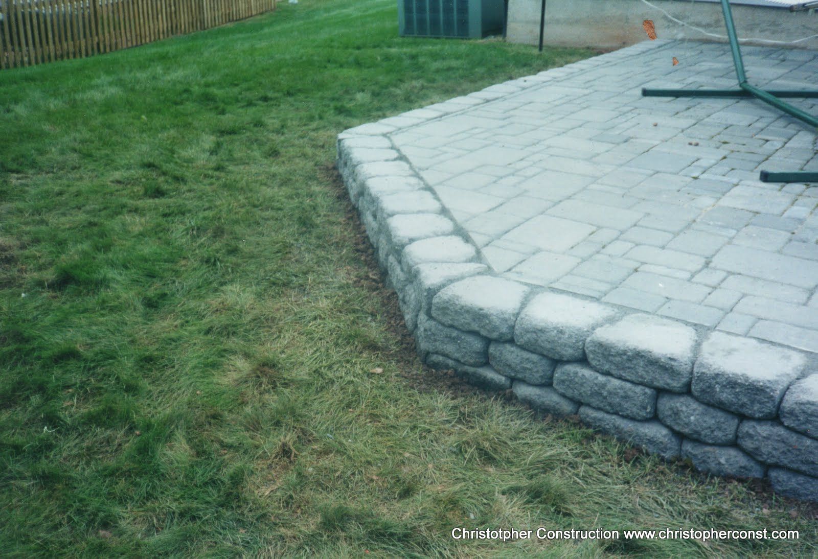 Curved stone patio edge beside a grassy yard and wooden fence