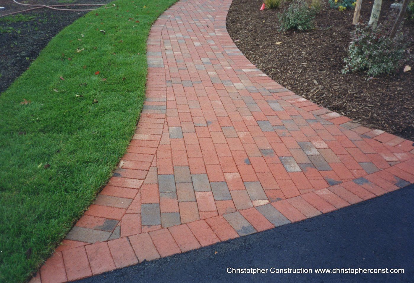 Curving brick garden path bordered by green lawn and mulch beds