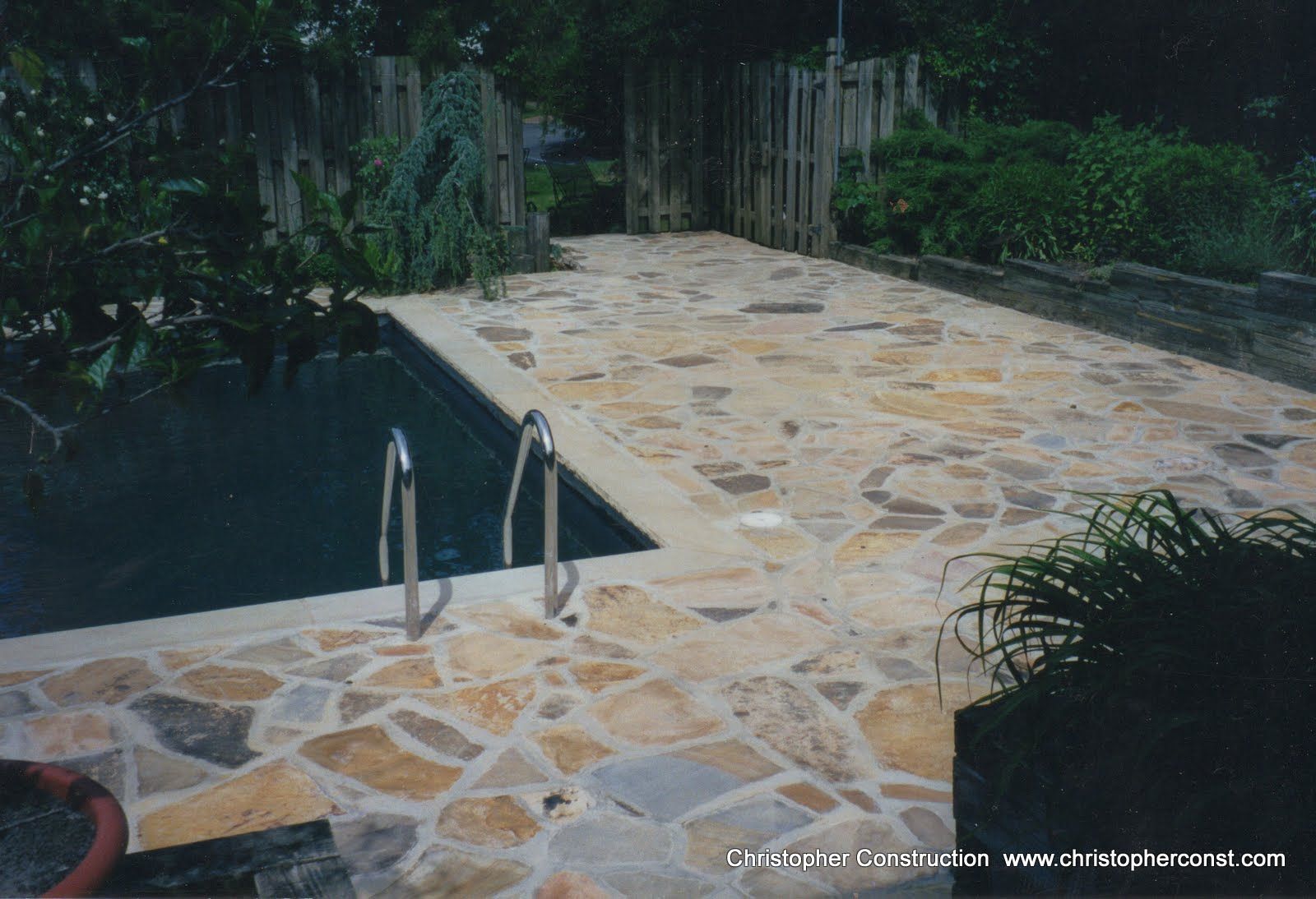 Stone pool deck with metal handrails beside dark water and green shrubs