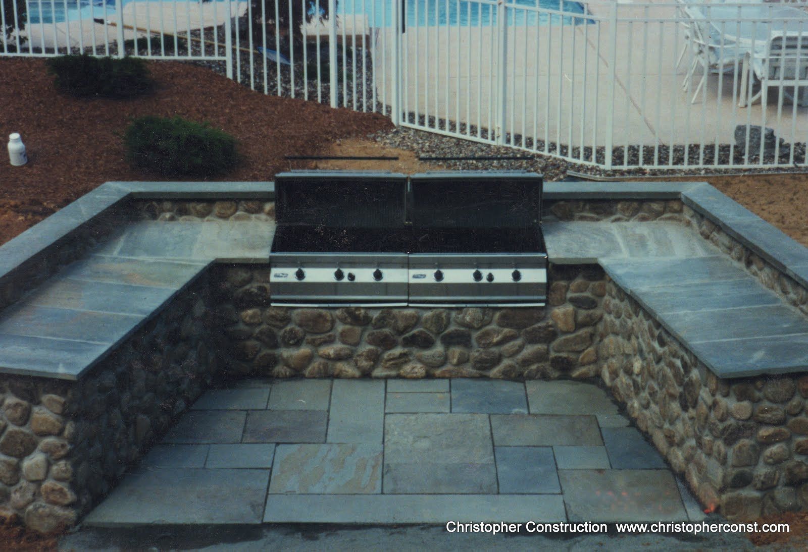 Outdoor brick fire pit with stone seating on both sides and a paved patio area