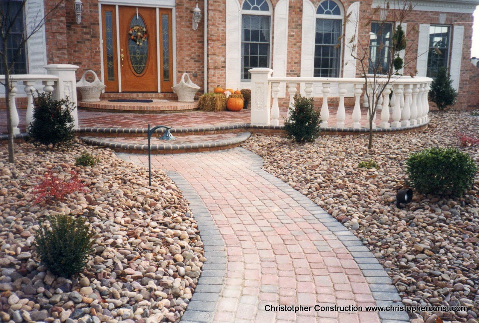 Brick walkway leading to a front door with steps, flanked by stone landscaping and small shrubs