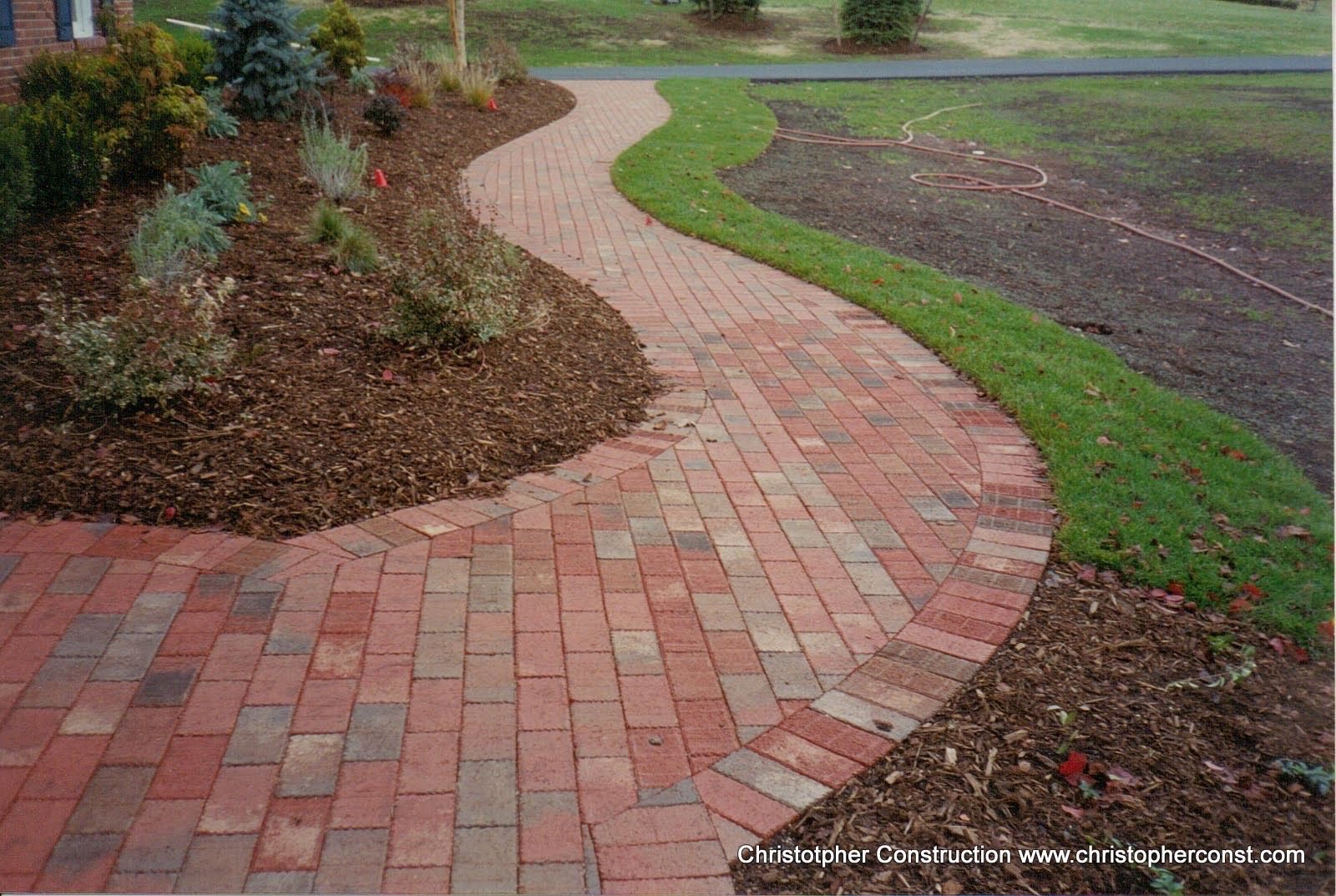 Curved red brick walkway through a landscaped garden beside a grassy path