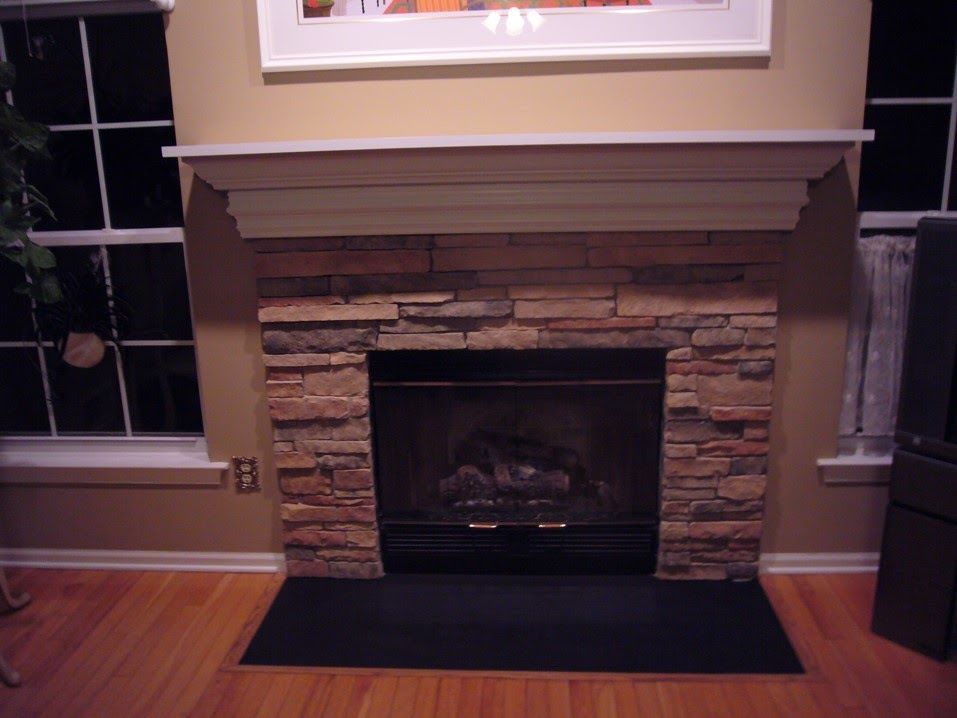 Stone fireplace with dark firebox and black hearth in a living room, flanked by windows and hardwood floor