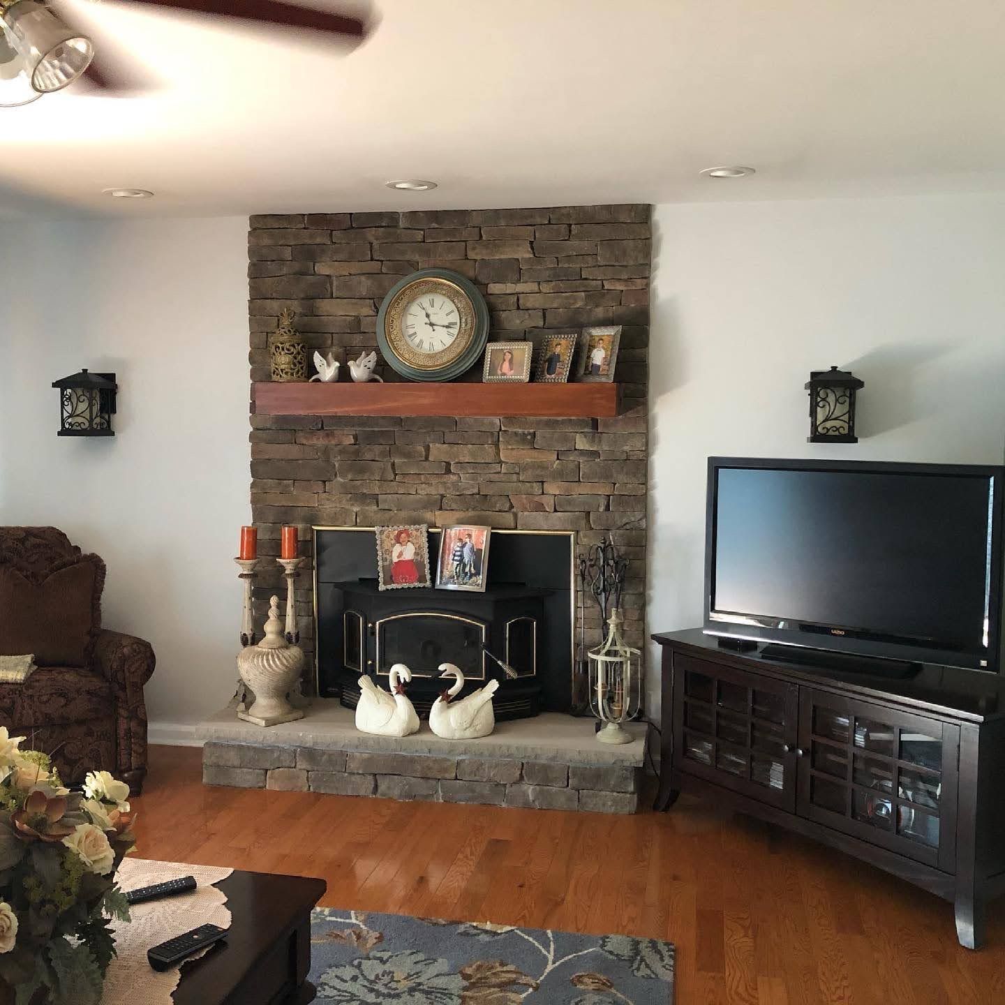 Living room with stone fireplace, clock and decor, dark TV console, hardwood floor, and brown armchair