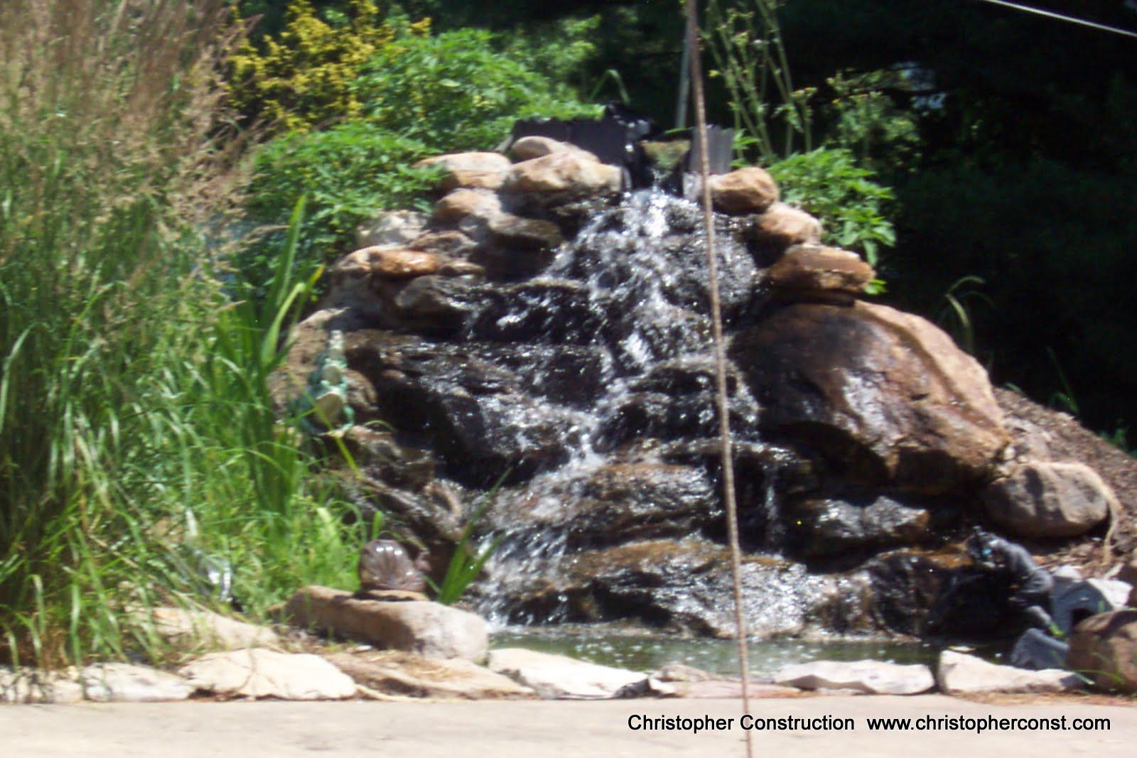 Small rock waterfall in a garden, with water flowing over stacked stones and green plants around it