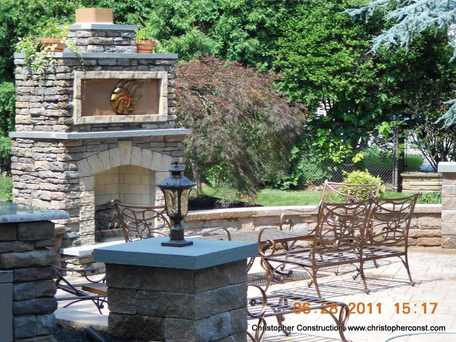 Stone outdoor fireplace with bench seating in a leafy garden patio