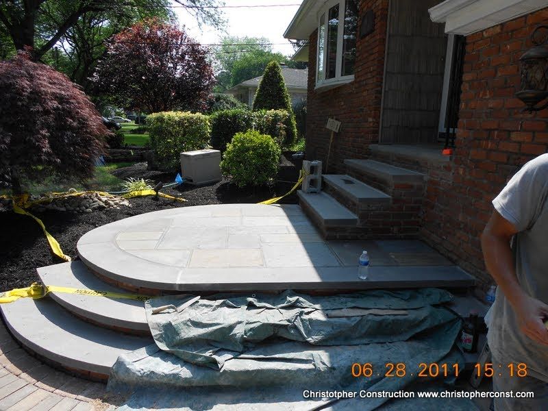 Backyard patio with curved stone steps and a brick house entrance under construction