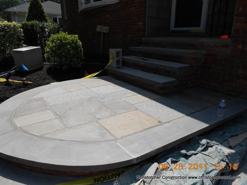 Small curved stone patio under construction beside brick steps, with tools and a water bottle nearby