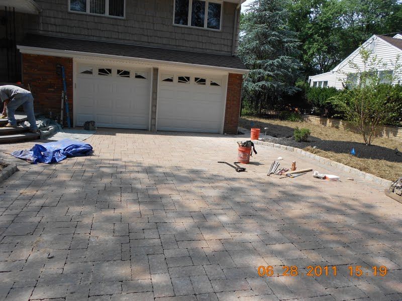 Driveway with pavers in front of a two-car garage, with tools and materials laid out for work.