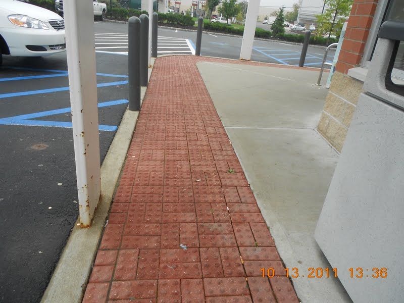 Brick sidewalk ramp beside parking spaces and building entrance, with curb cuts and metal posts.