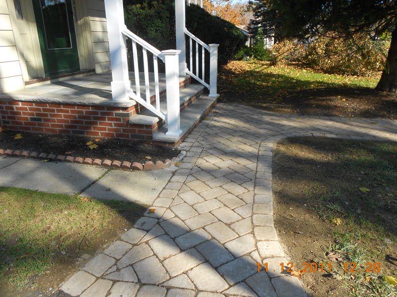 Brick house porch with white railing and a curved stone walkway in a sunny yard