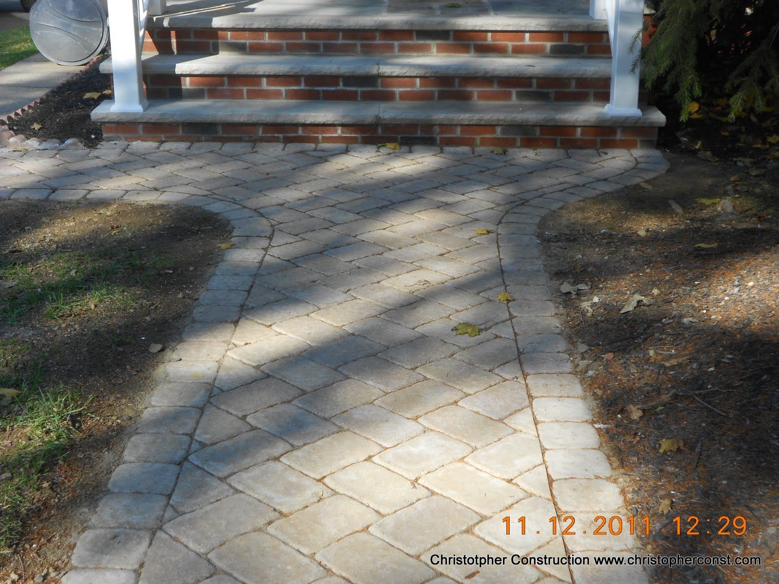 Stone walkway leading to brick steps at a house entrance, bordered by mulch and bushes