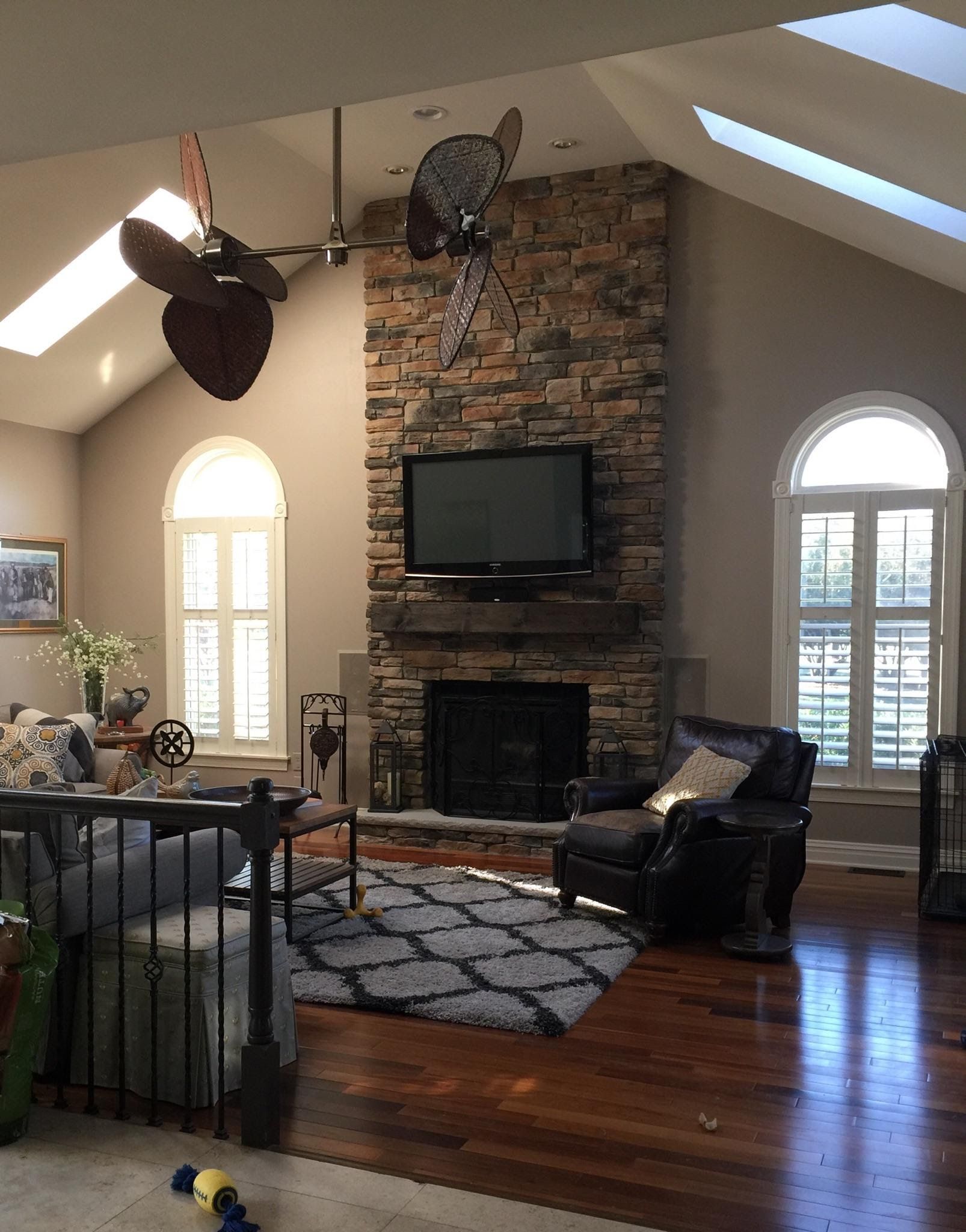 Living room with stone fireplace, mounted TV, leather chair, hardwood floors, and vaulted ceiling with skylights