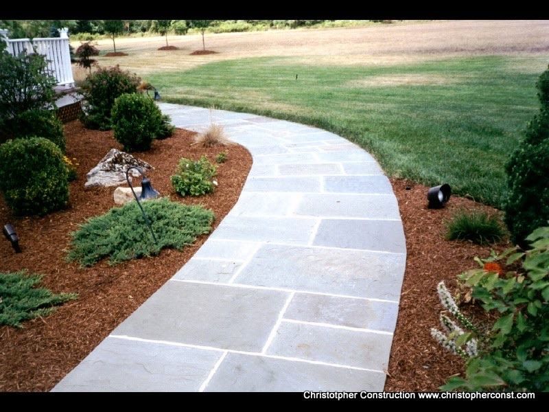 Curved stone walkway through a landscaped garden with shrubs and lawn