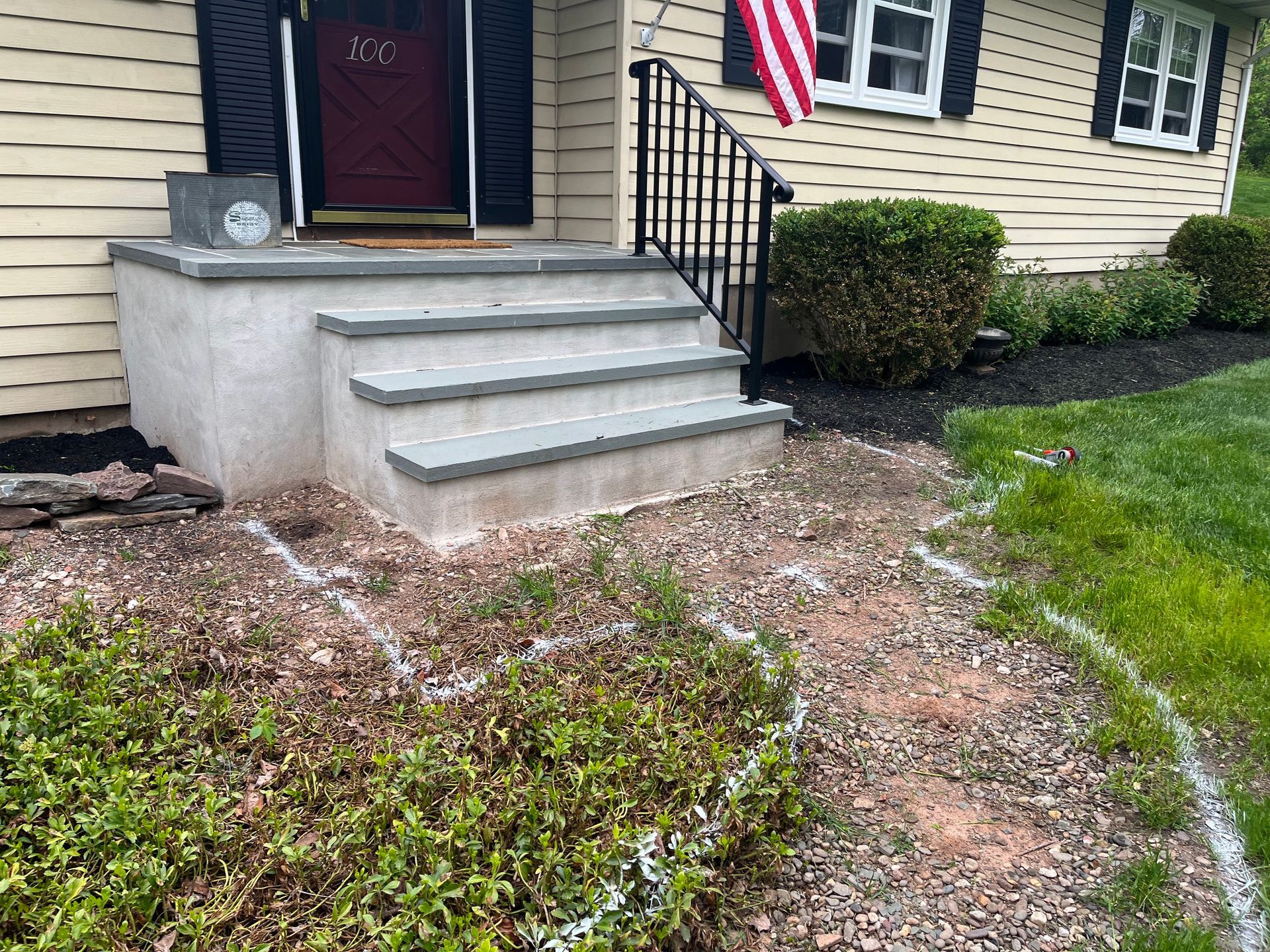 Front steps and walkway beside a house, with a small shrub and American flag.