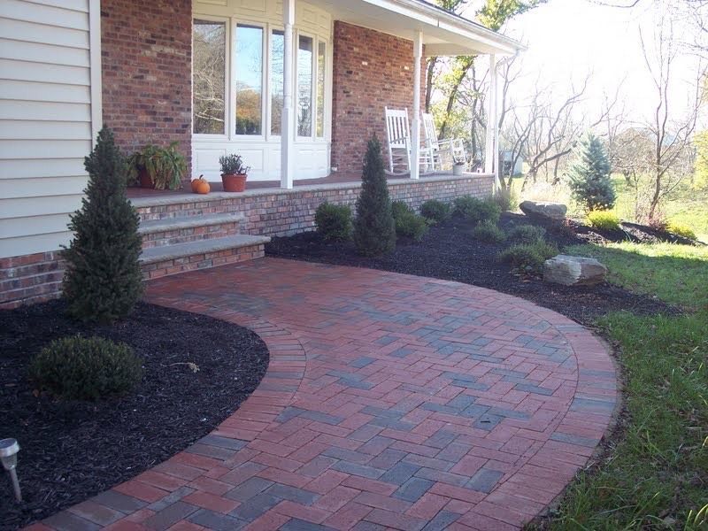 Curved red-brick walkway leading to a house porch with shrubs and landscaping beds