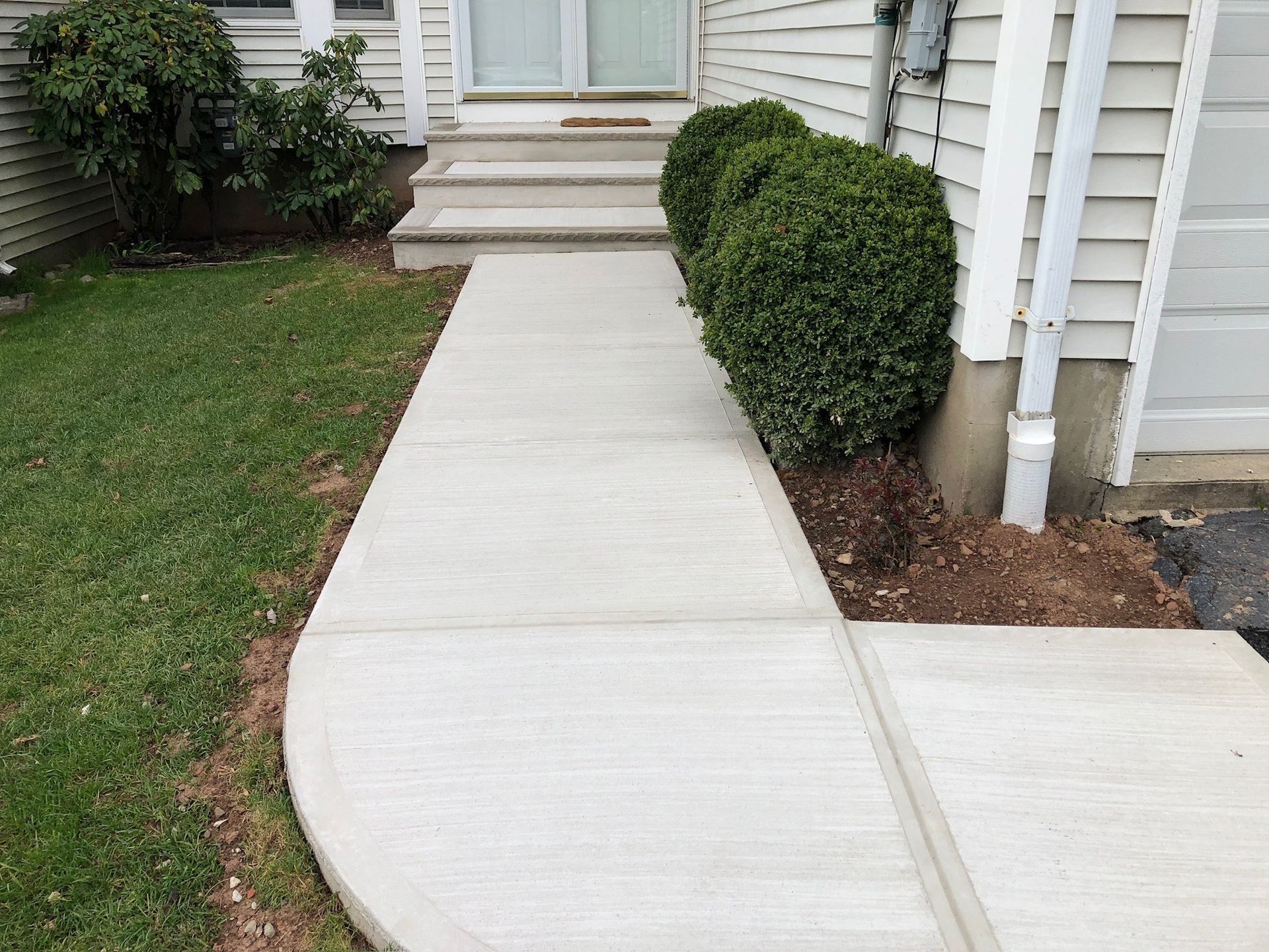 Concrete sidewalk path leading to a house entrance, bordered by grass and trimmed bushes