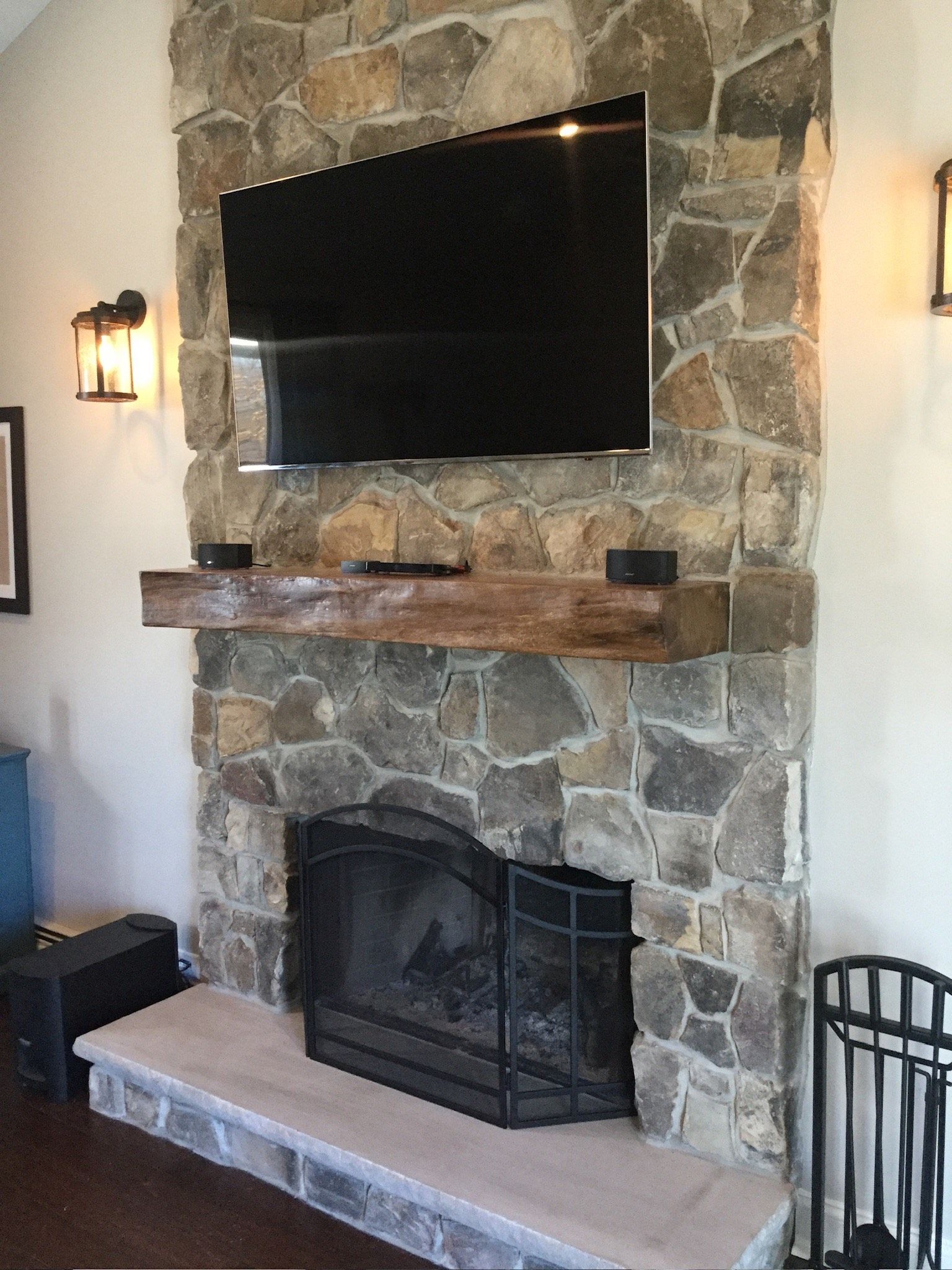 Stone fireplace with mounted TV, wooden mantel, and black screen insert in a living room