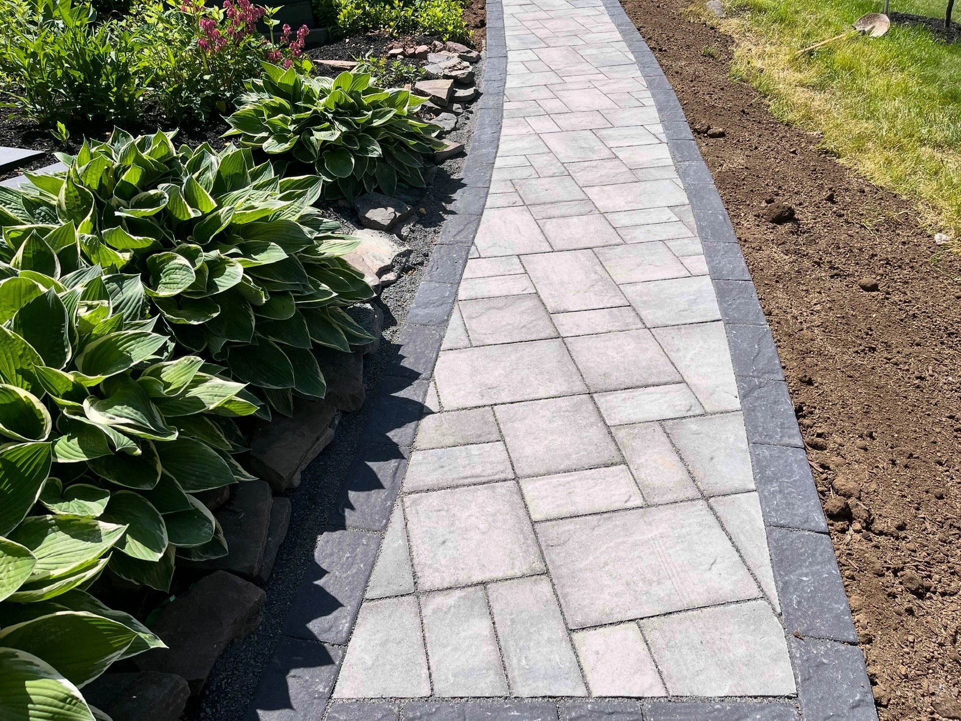 Stone garden path bordered by green plants and soil along a landscaped yard