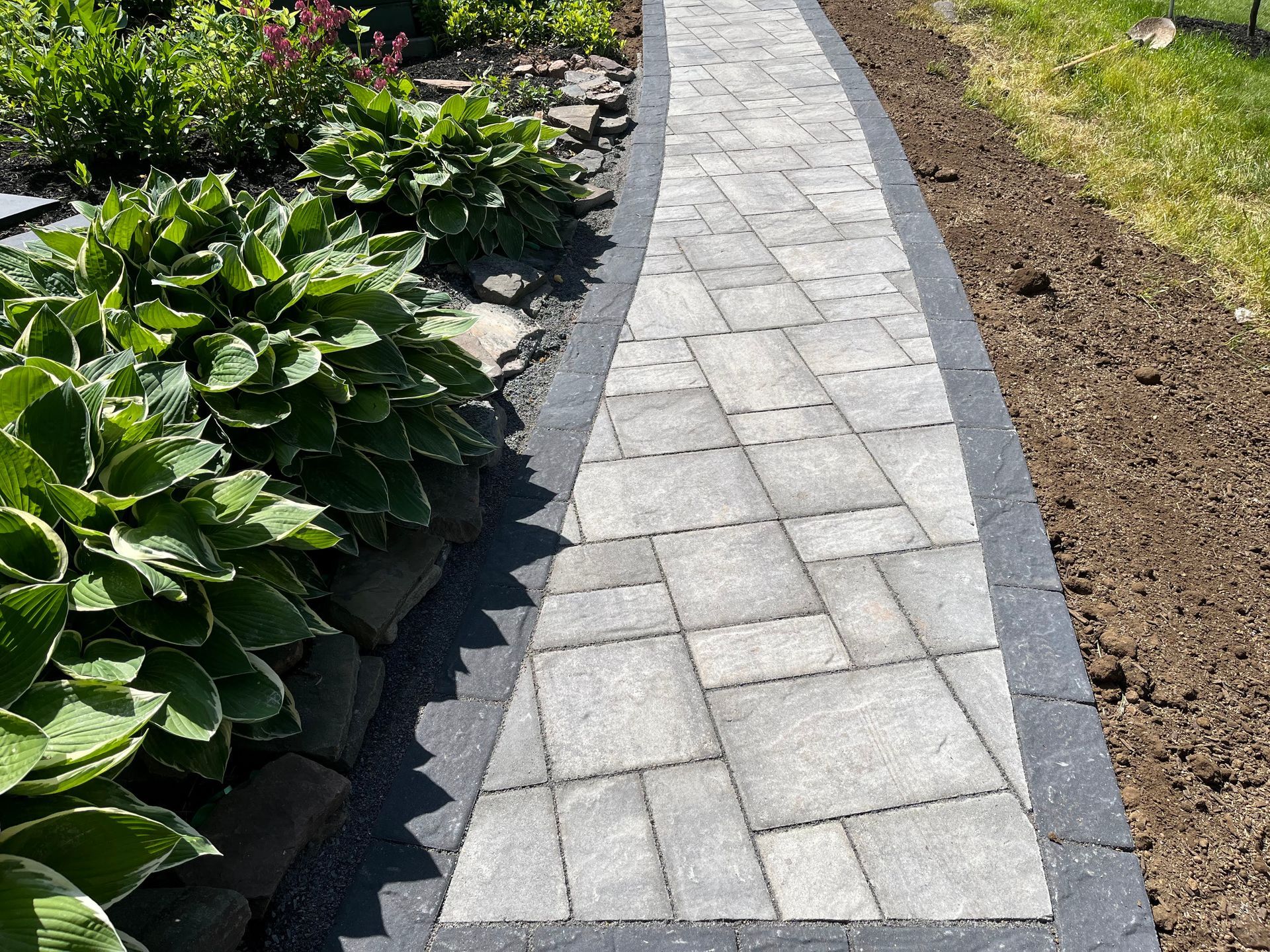 Curved gray stone walkway bordered by green plants and fresh soil