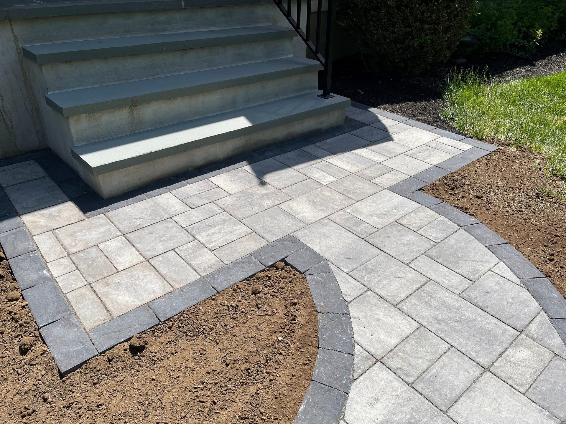 Curved stone paver walkway leading to concrete steps beside mulched garden beds