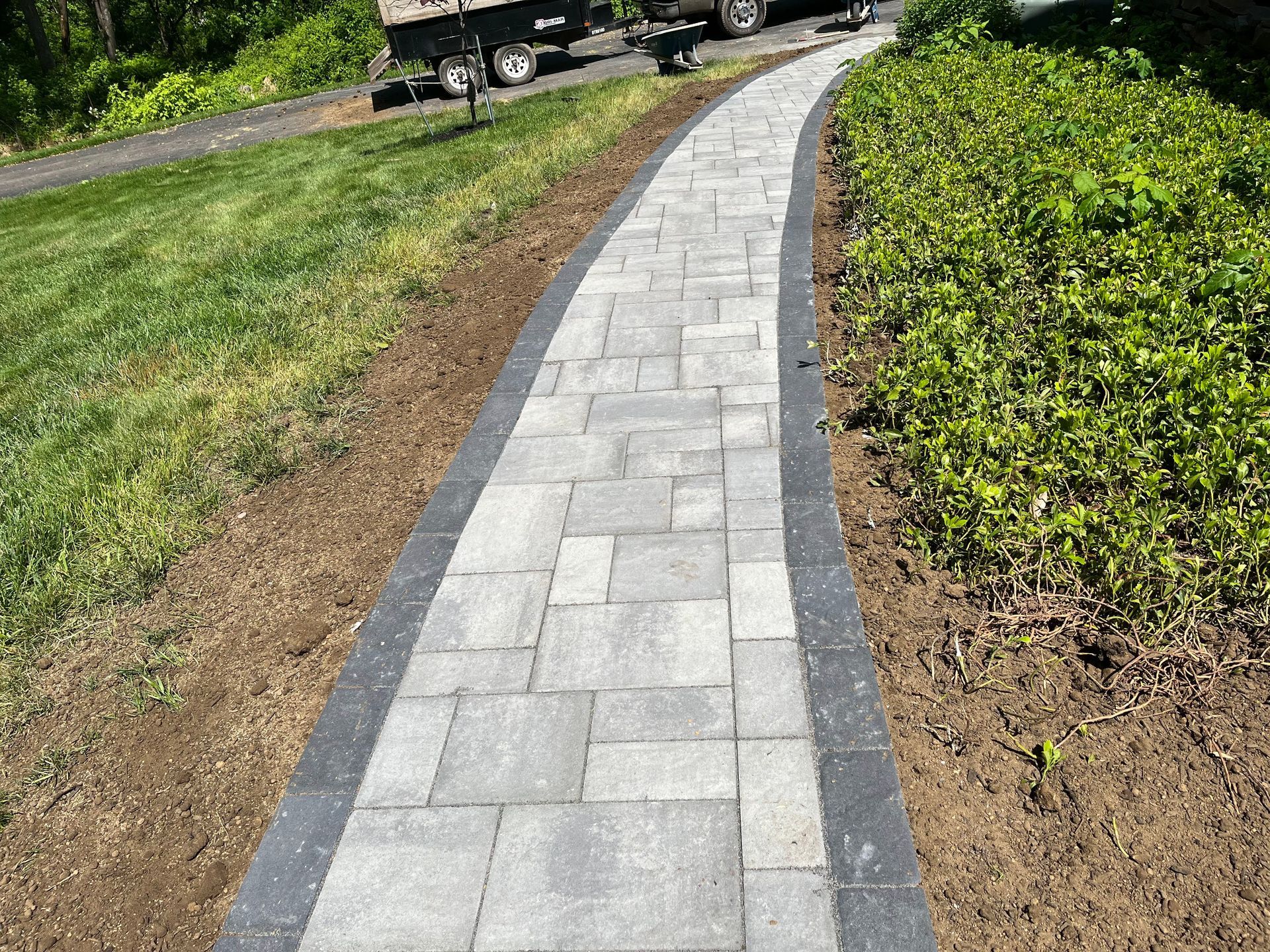 Curved gray stone walkway bordered by grass and shrubs