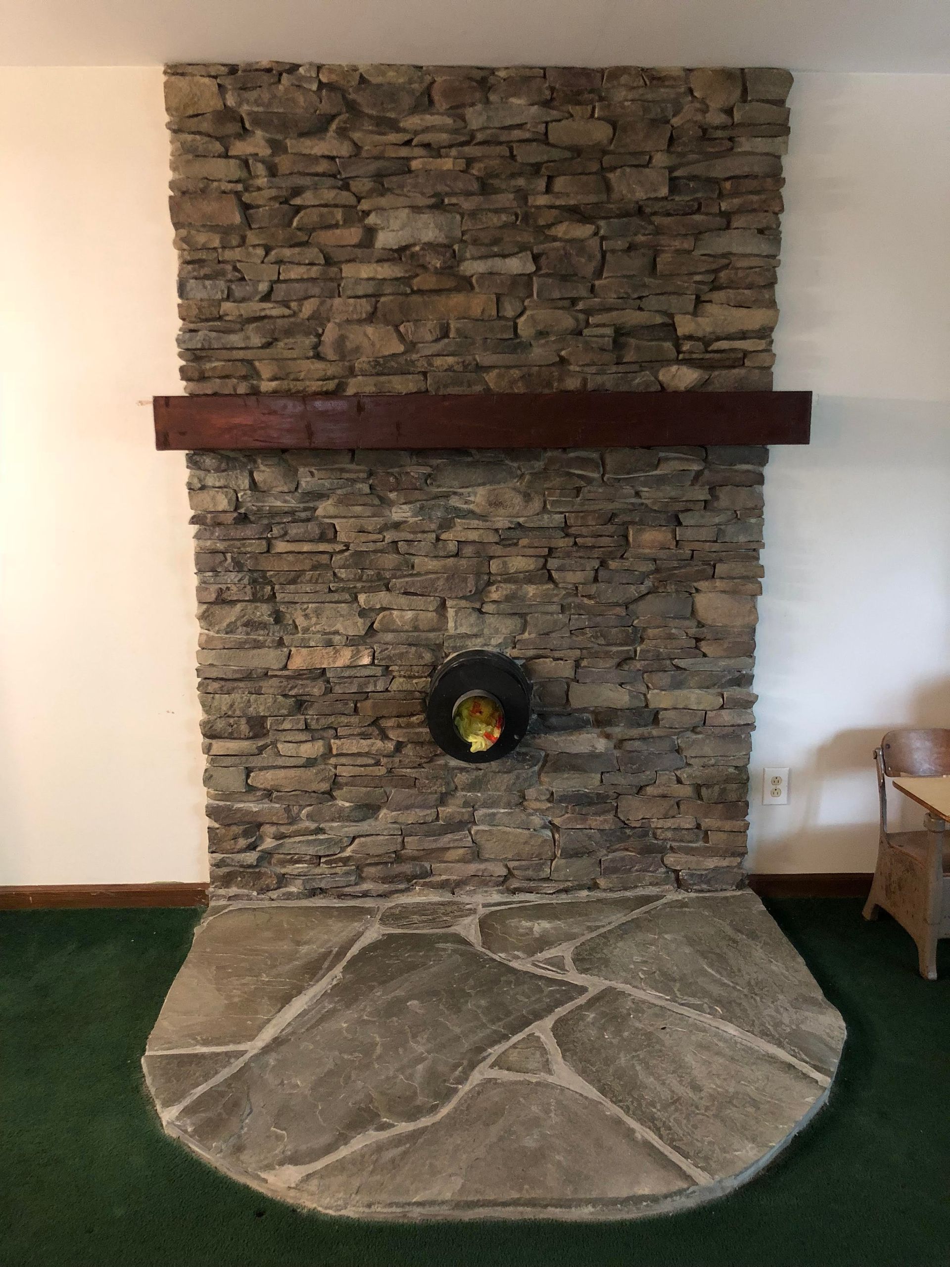 Stone fireplace with a dark wooden mantel and curved stone hearth in a living room.