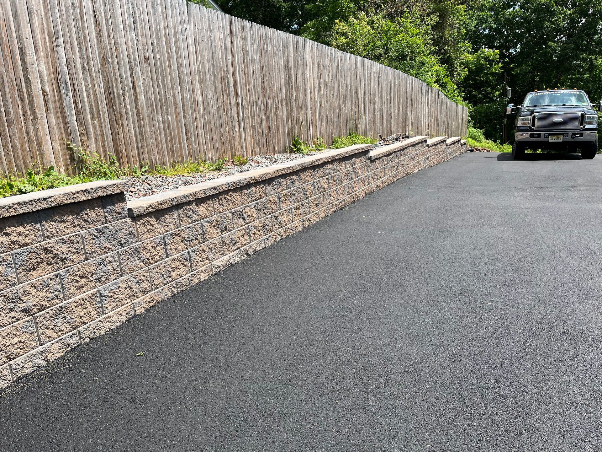 Long stone retaining wall beside a paved driveway, with a parked car at the end