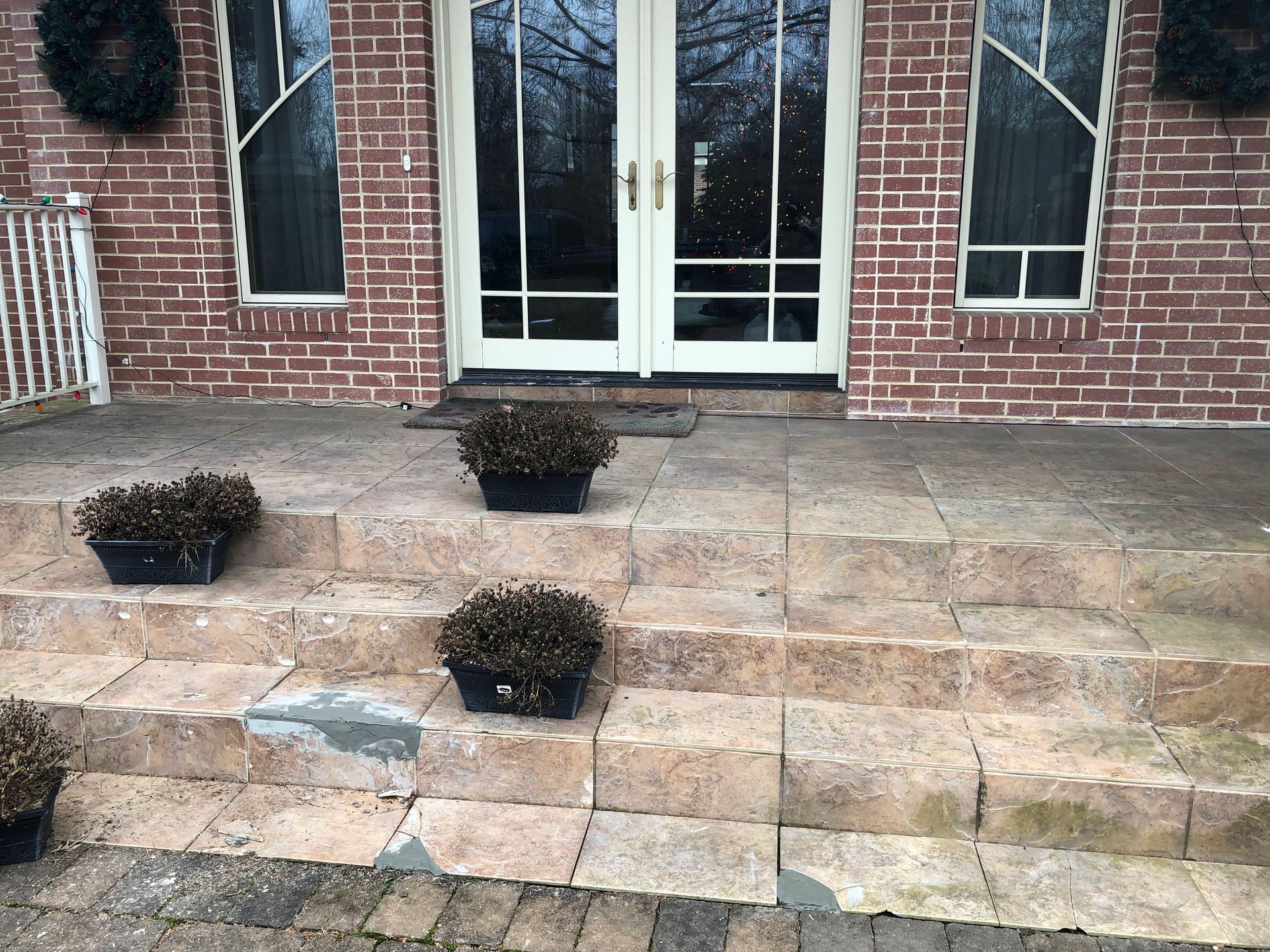 Brick house entrance with white double doors and three small potted shrubs on stone steps