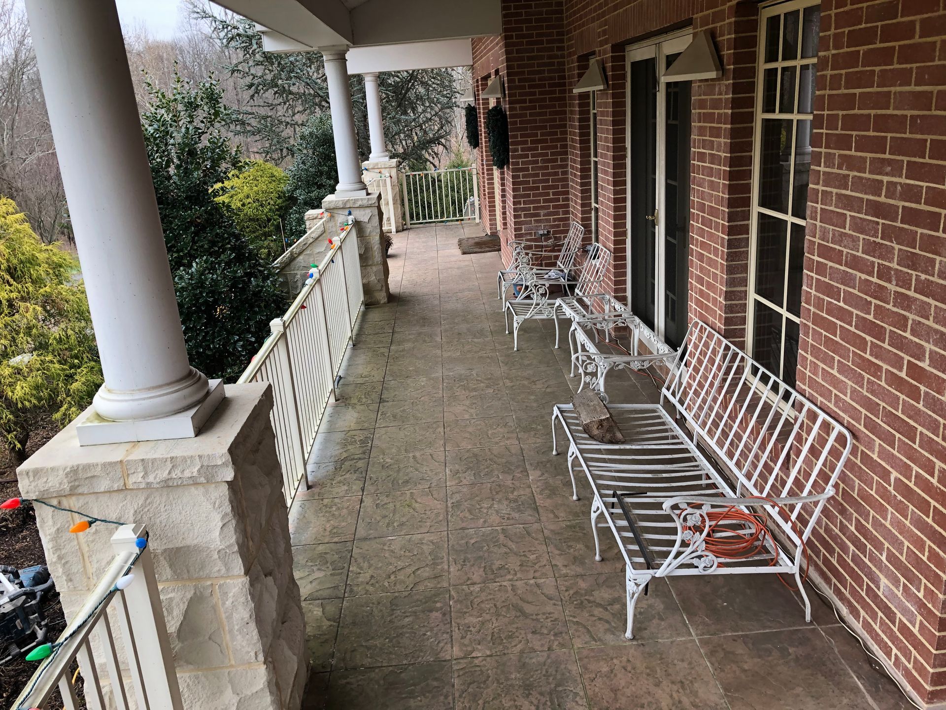 Covered brick porch with white columns, benches, and a railing overlooking trees.