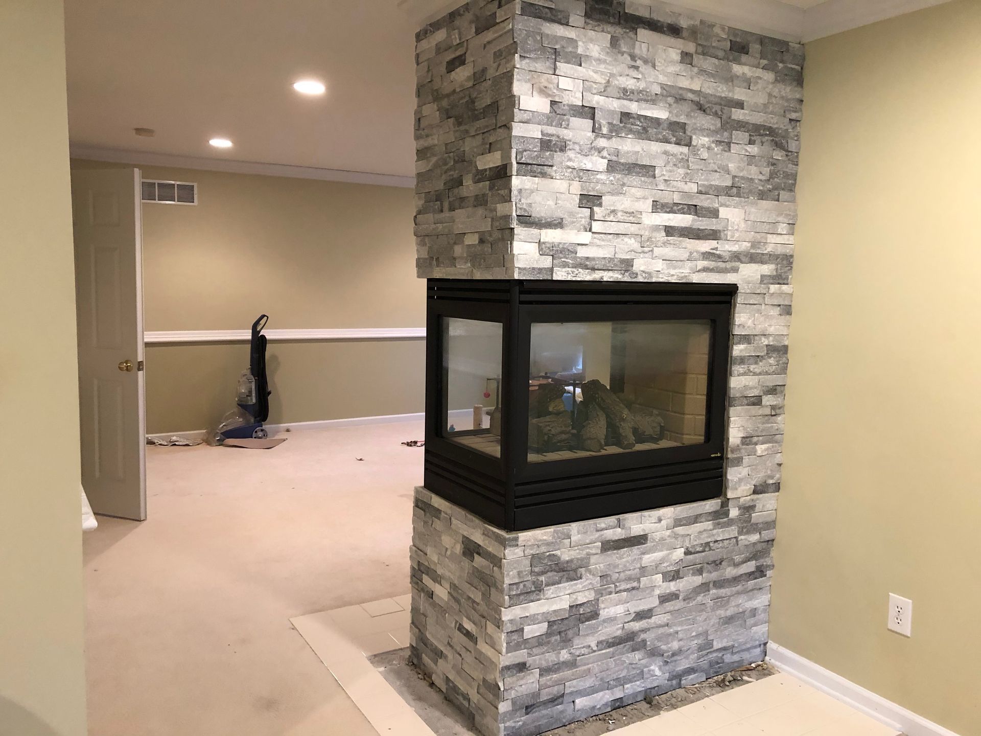 Living room with stone fireplace, beige walls, and carpeted open floor area