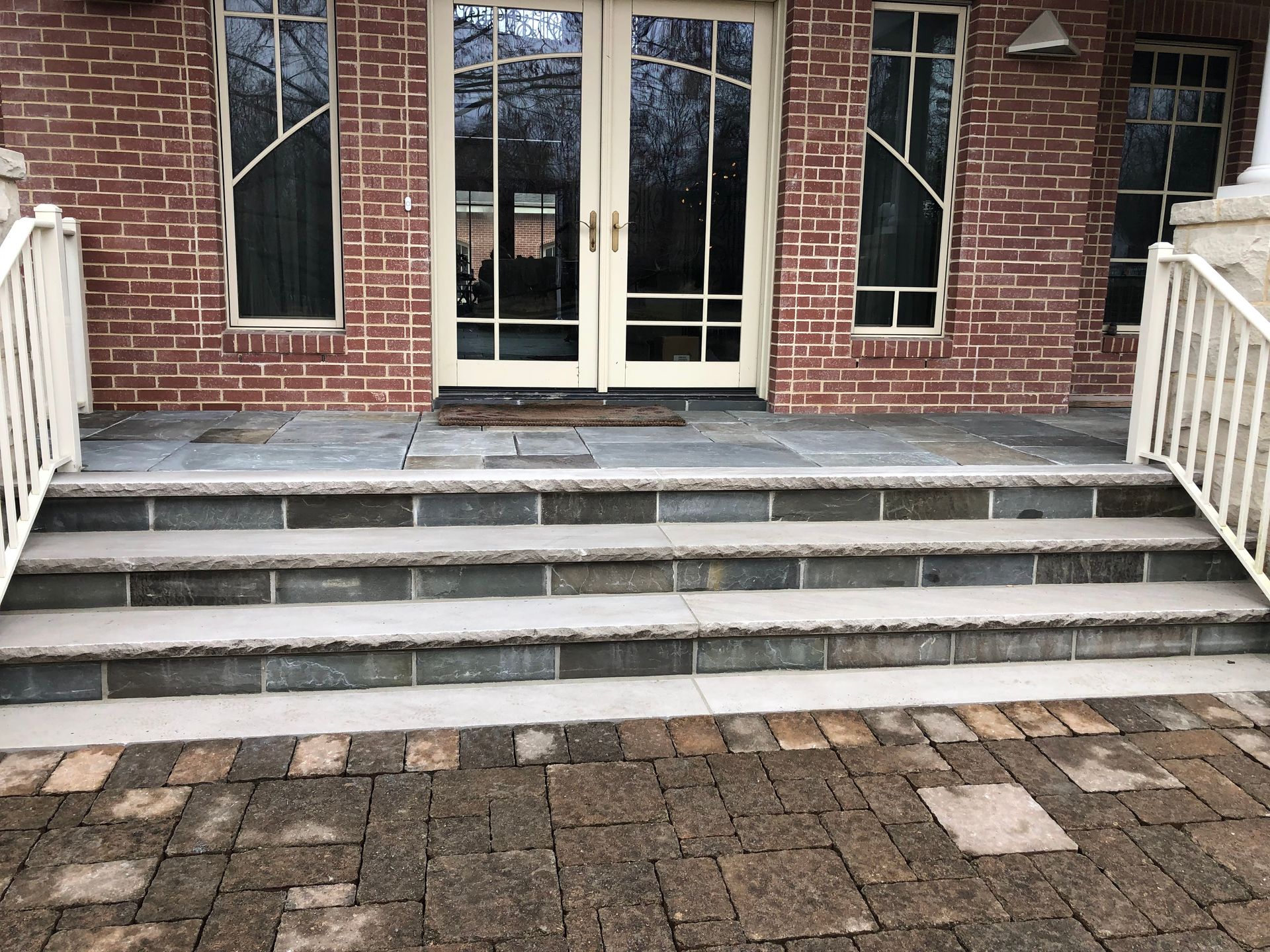 Brick building entrance with steps, white railings, and double glass doors