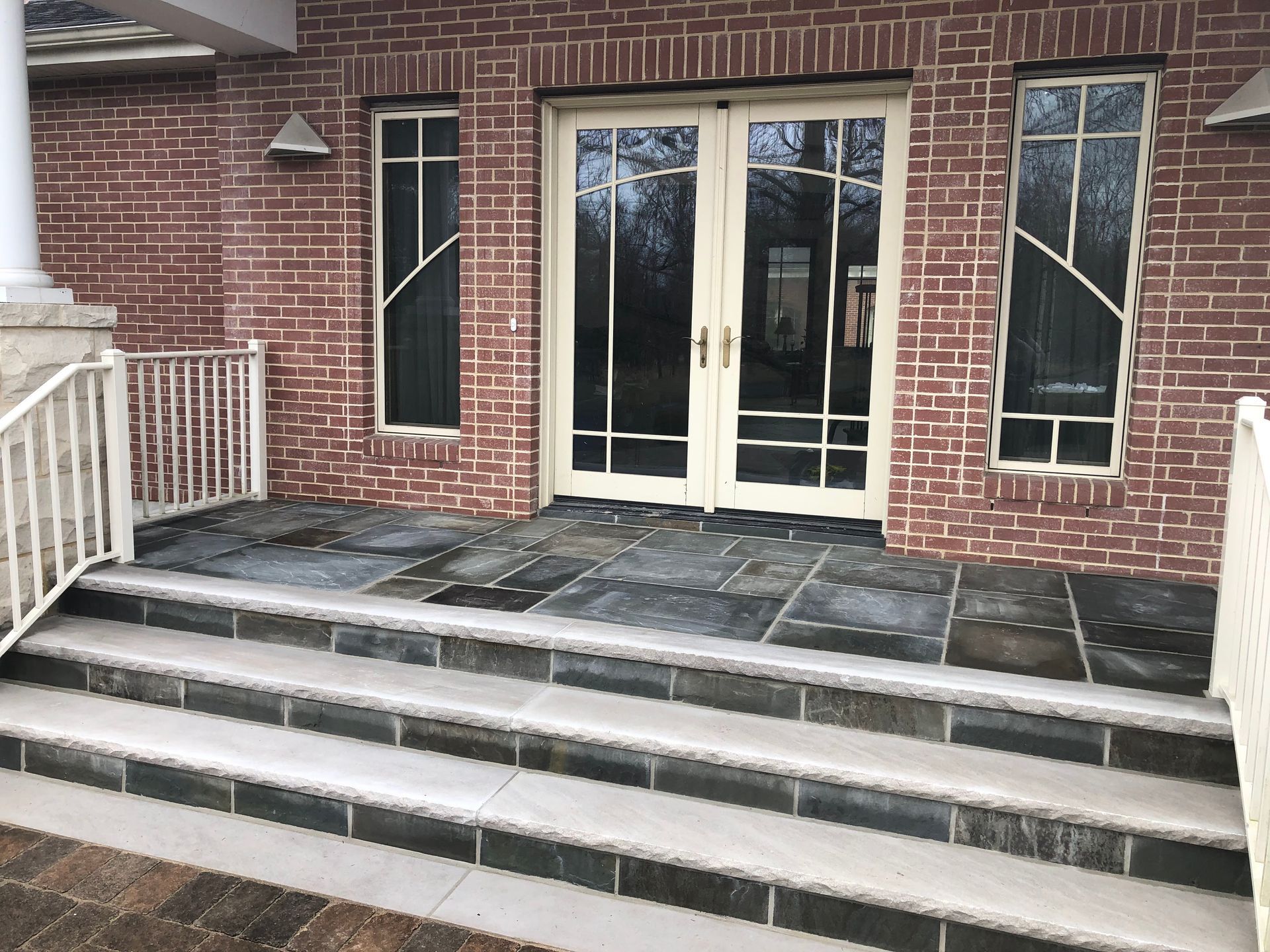 Snow-dusted front steps leading to glass double doors on a brick building