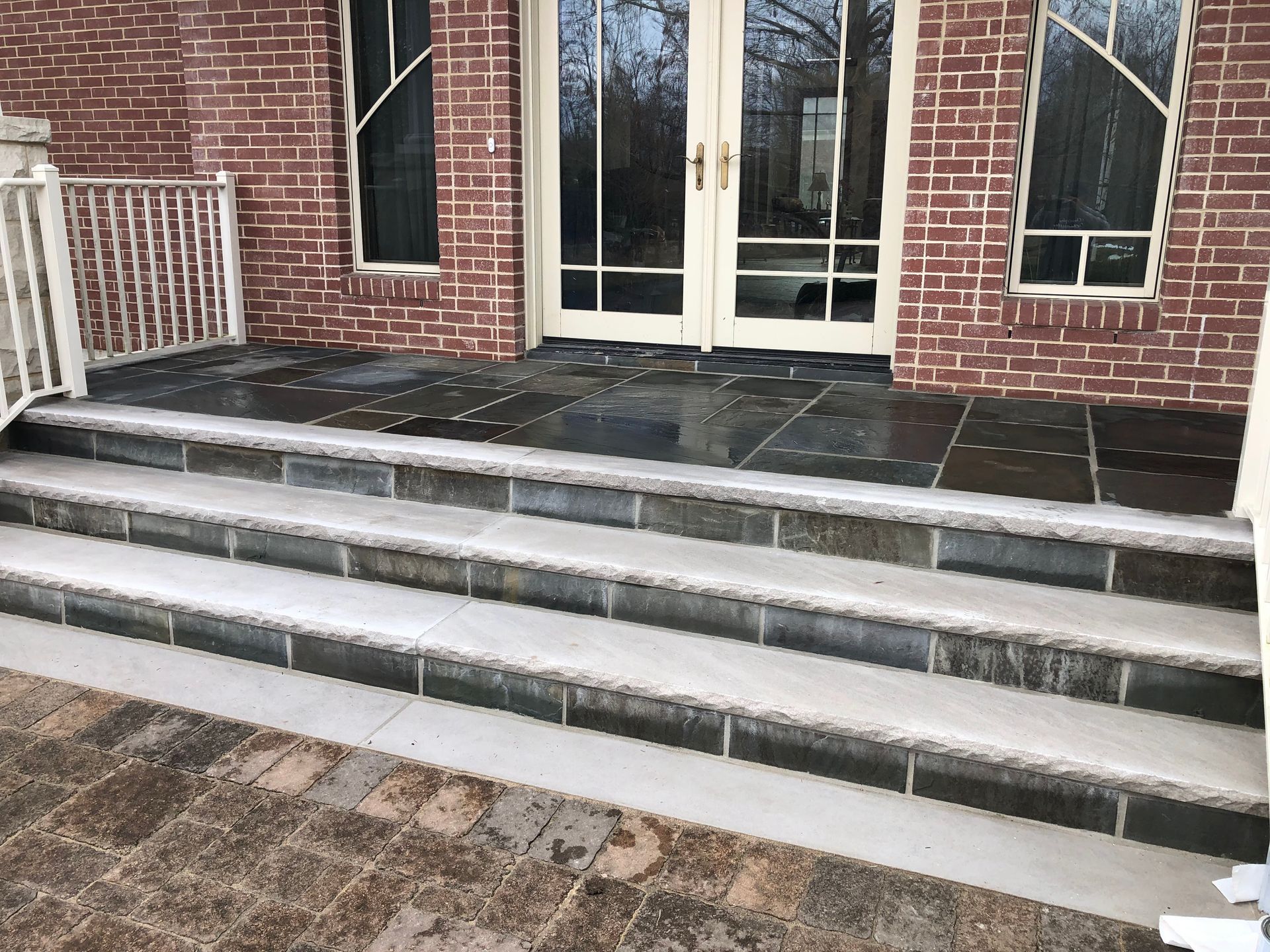 Brick building entrance with double glass doors and wide concrete steps with dark stone landing