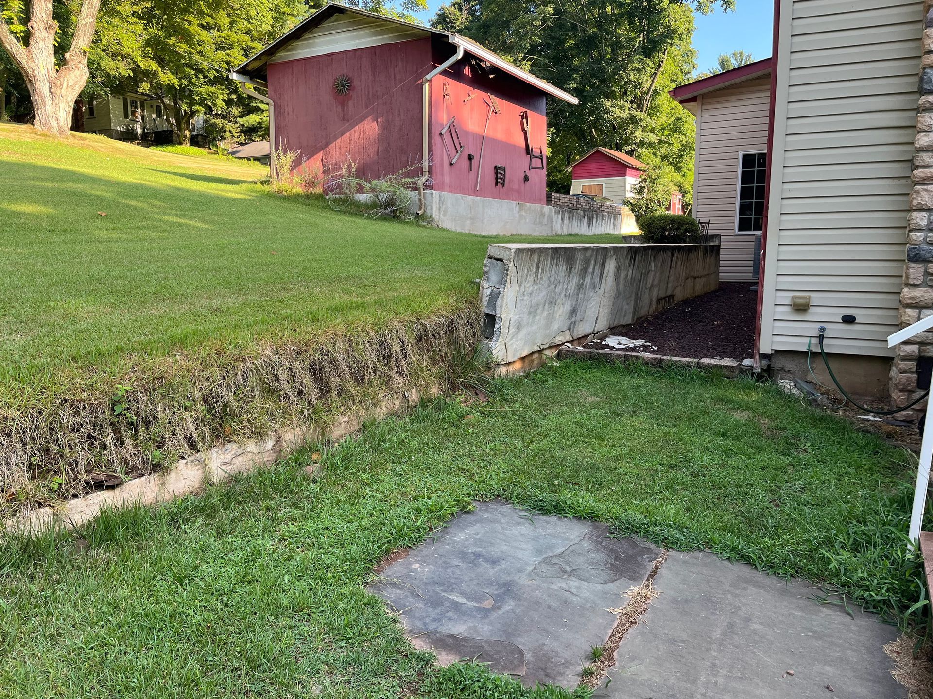 Grassy backyard with concrete patio, retaining wall, and red shed near a house.