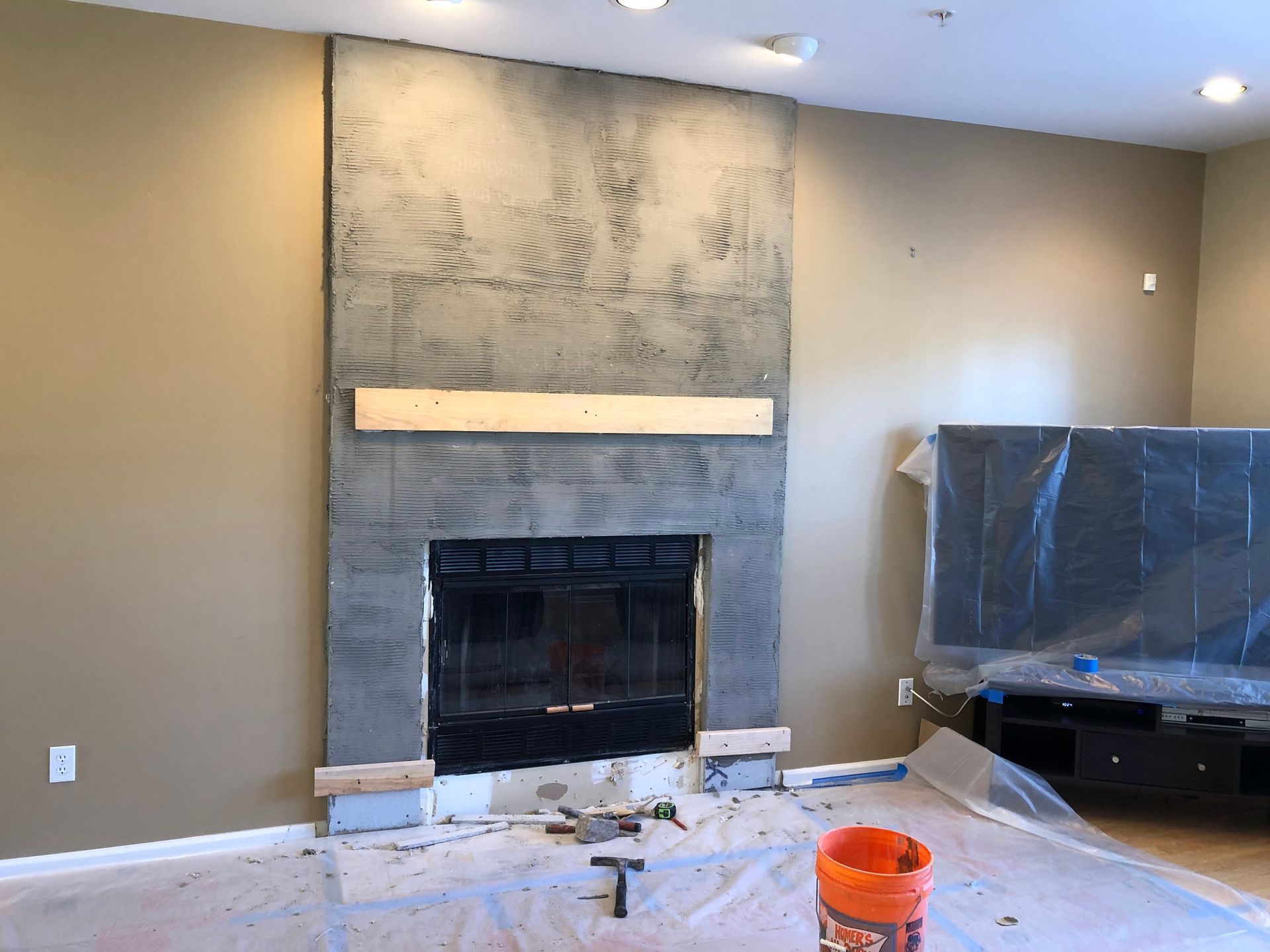 Living room with unfinished fireplace, gray wall, plastic-covered TV, and renovation debris on the floor