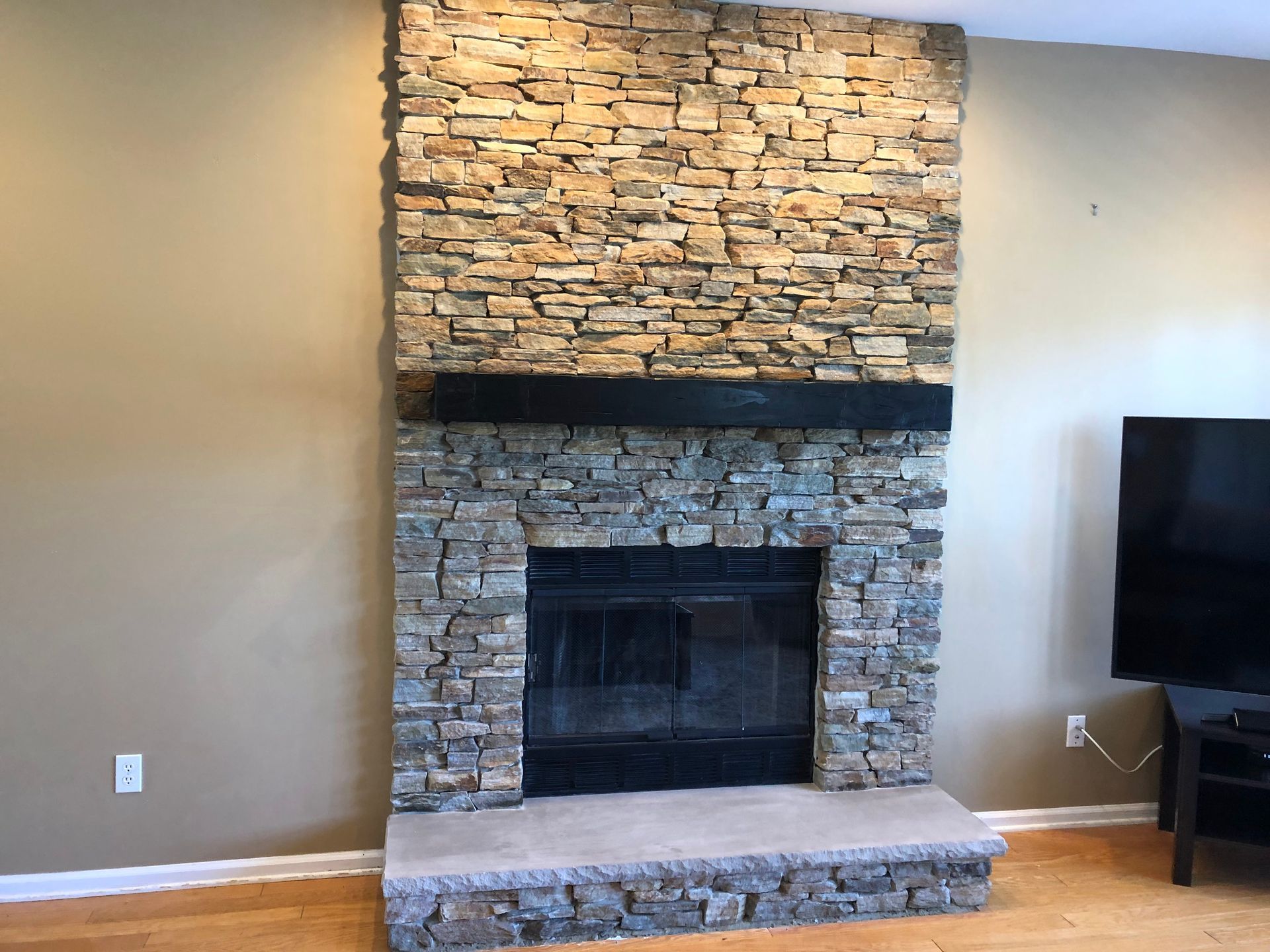 Stone fireplace with a black firebox in a beige living room, with a stone hearth and partial TV visible on the right
