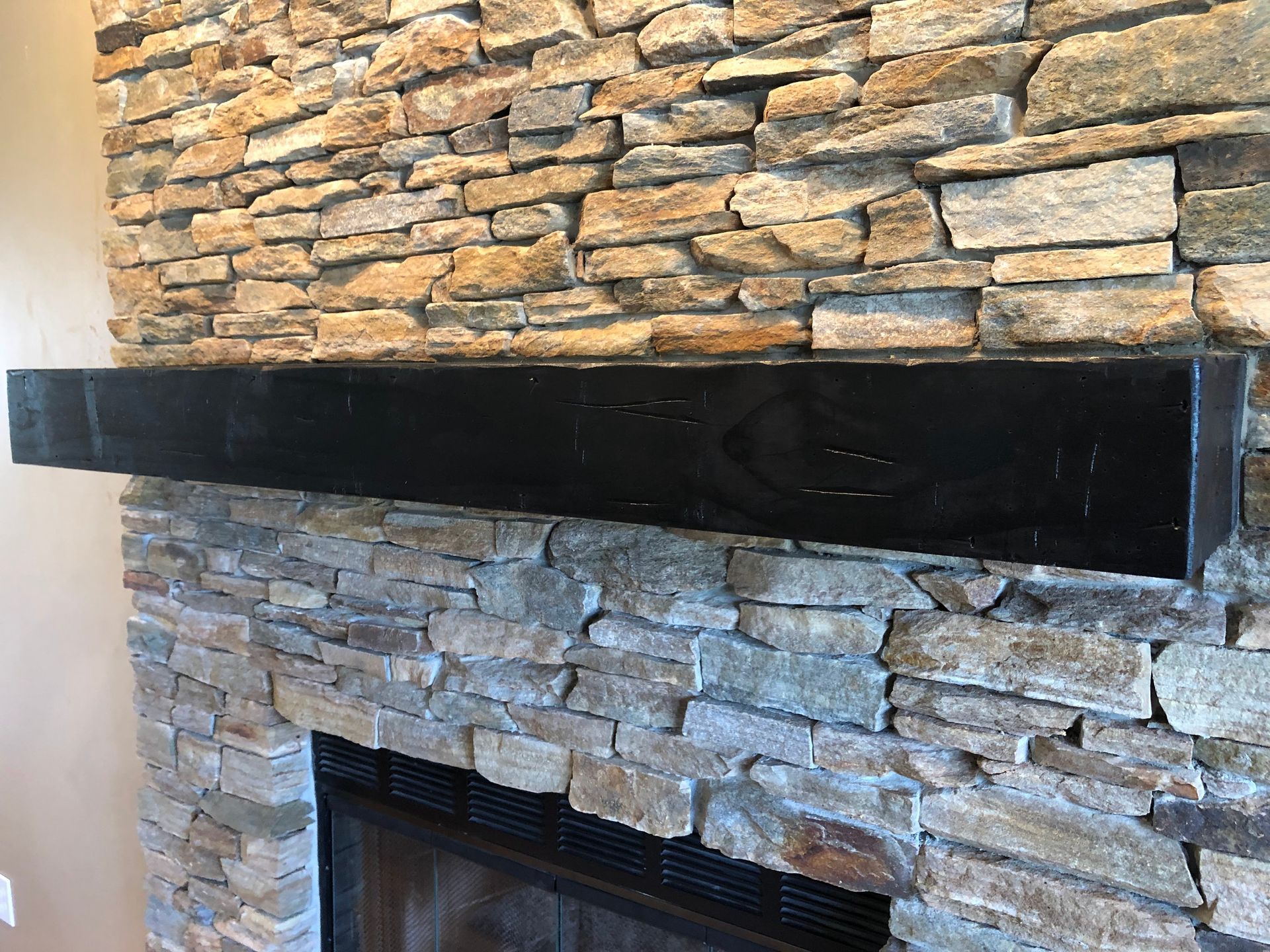 Stone fireplace with a black mantel and stacked stone wall surround