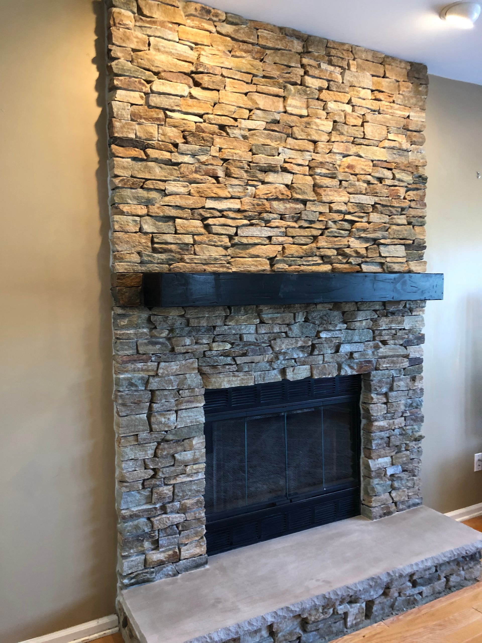 Stone fireplace with black mantle and raised stone hearth against a beige wall