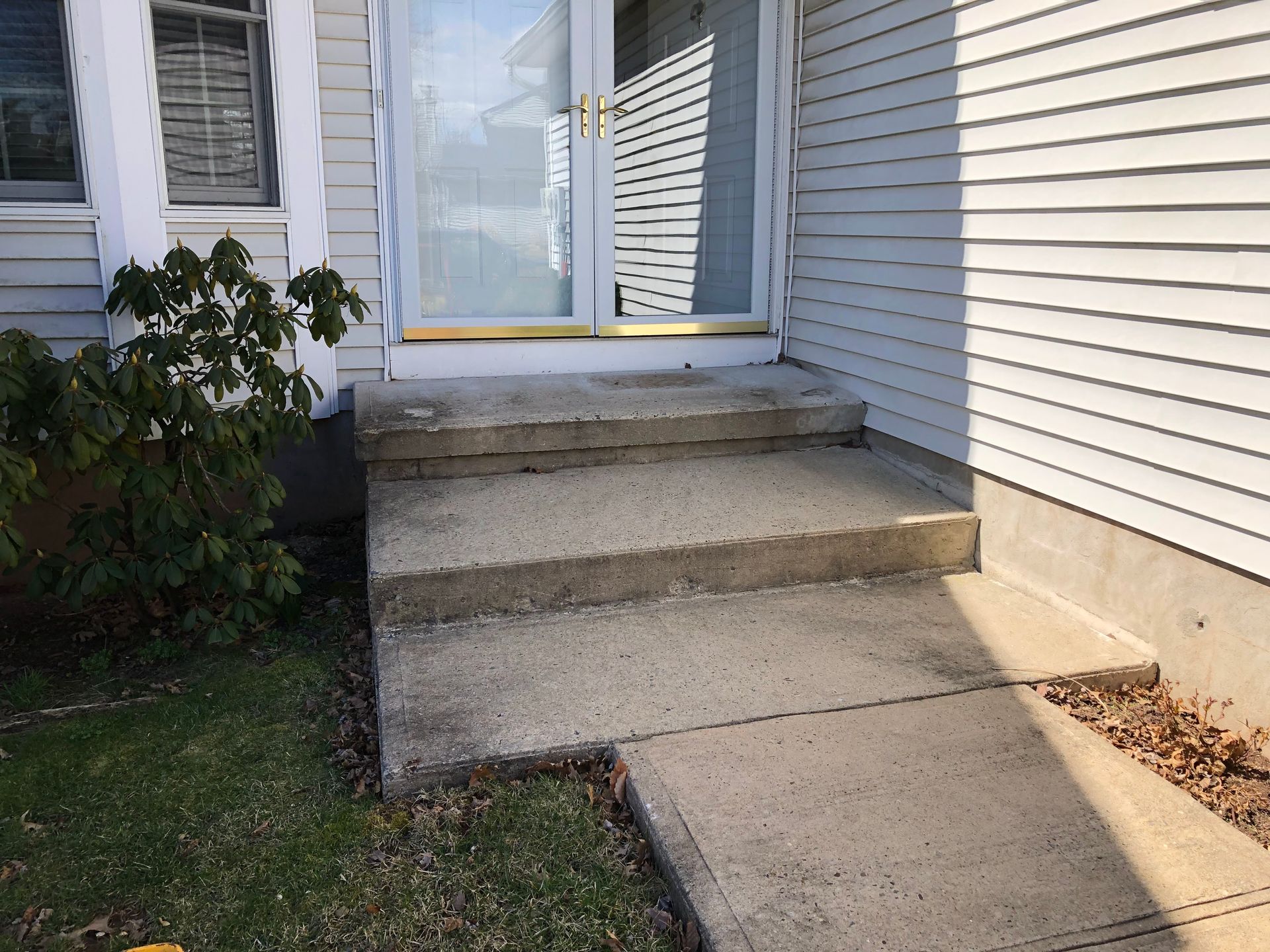 Concrete steps leading to a white house entrance with a short walkway and surrounding shrubs