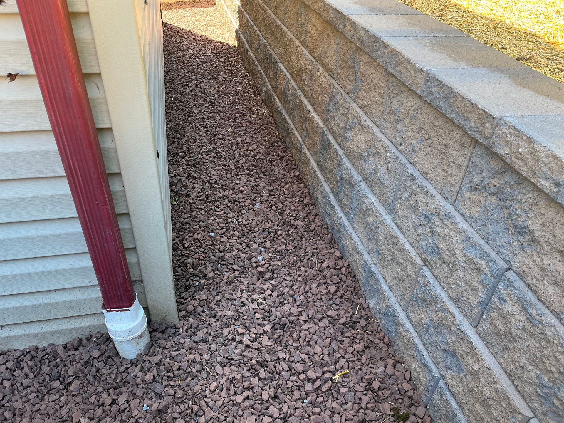 Narrow gravel path between a house siding and a cinder block wall