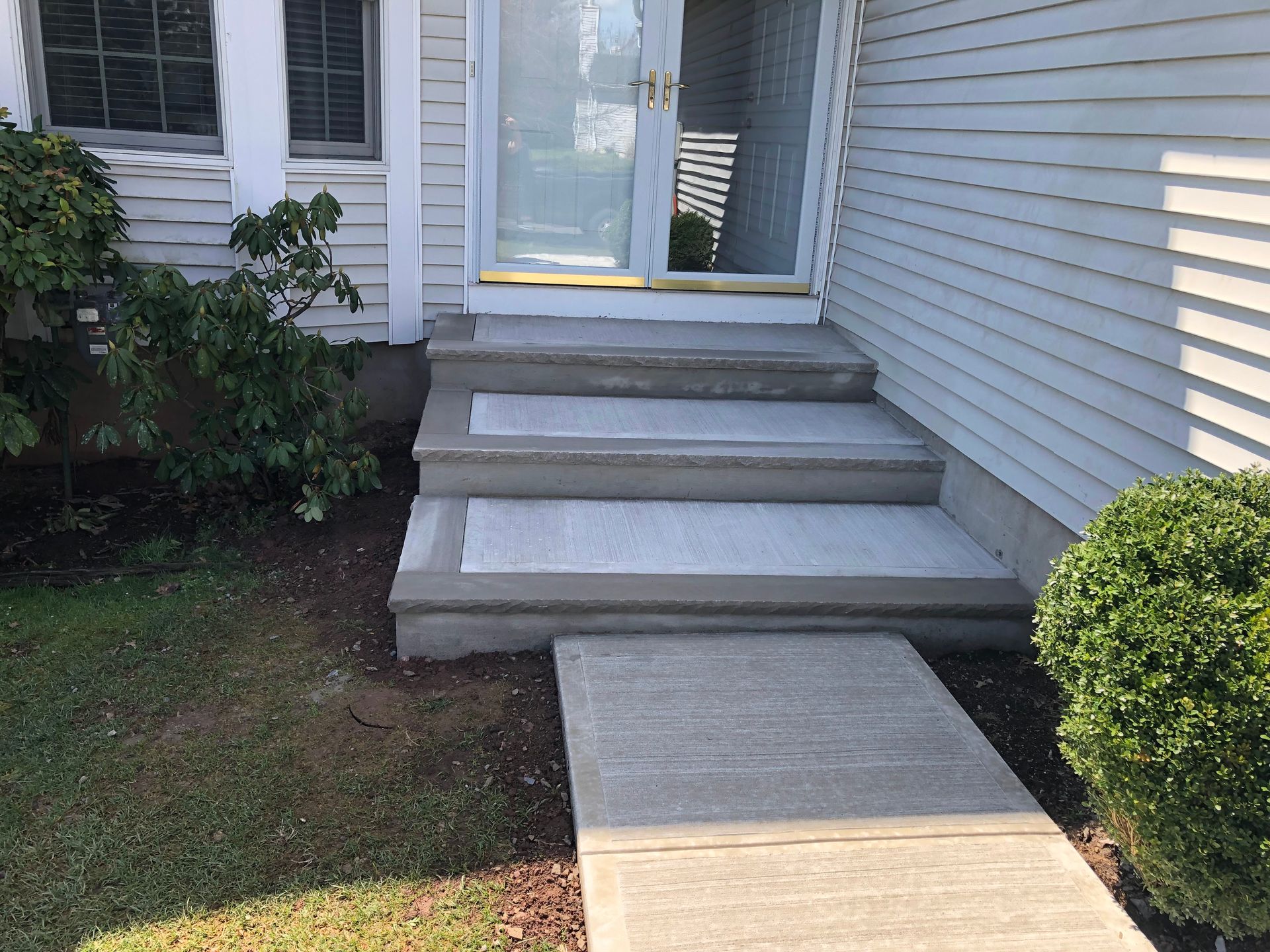 Front steps leading to a white house entrance with a concrete walkway and shrubs on both sides