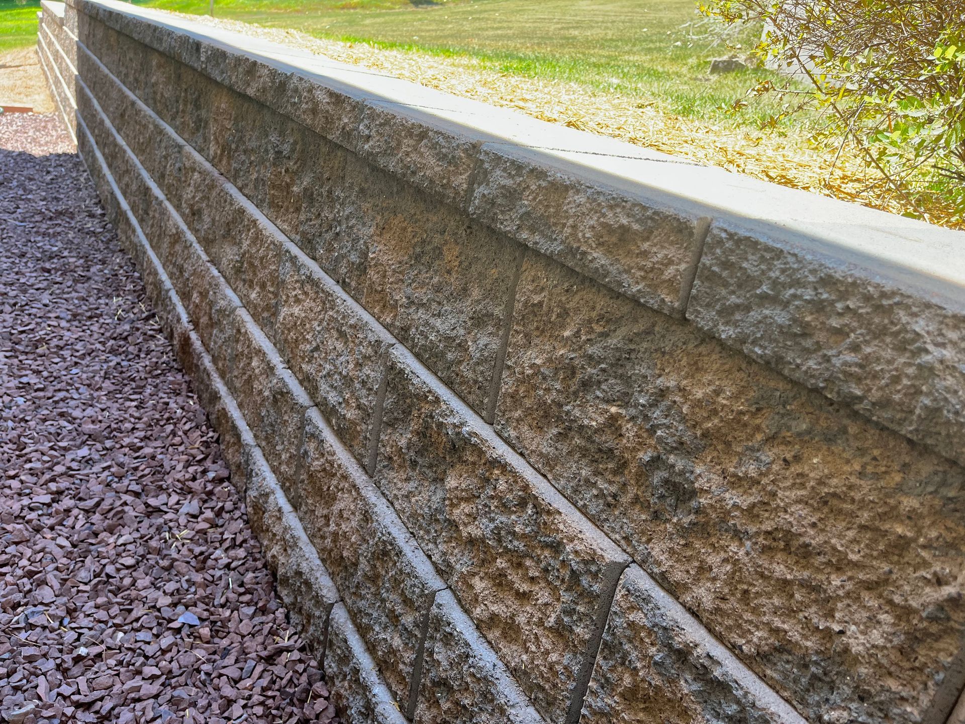 Textured stone retaining wall bordering a gravel path in a park-like area.