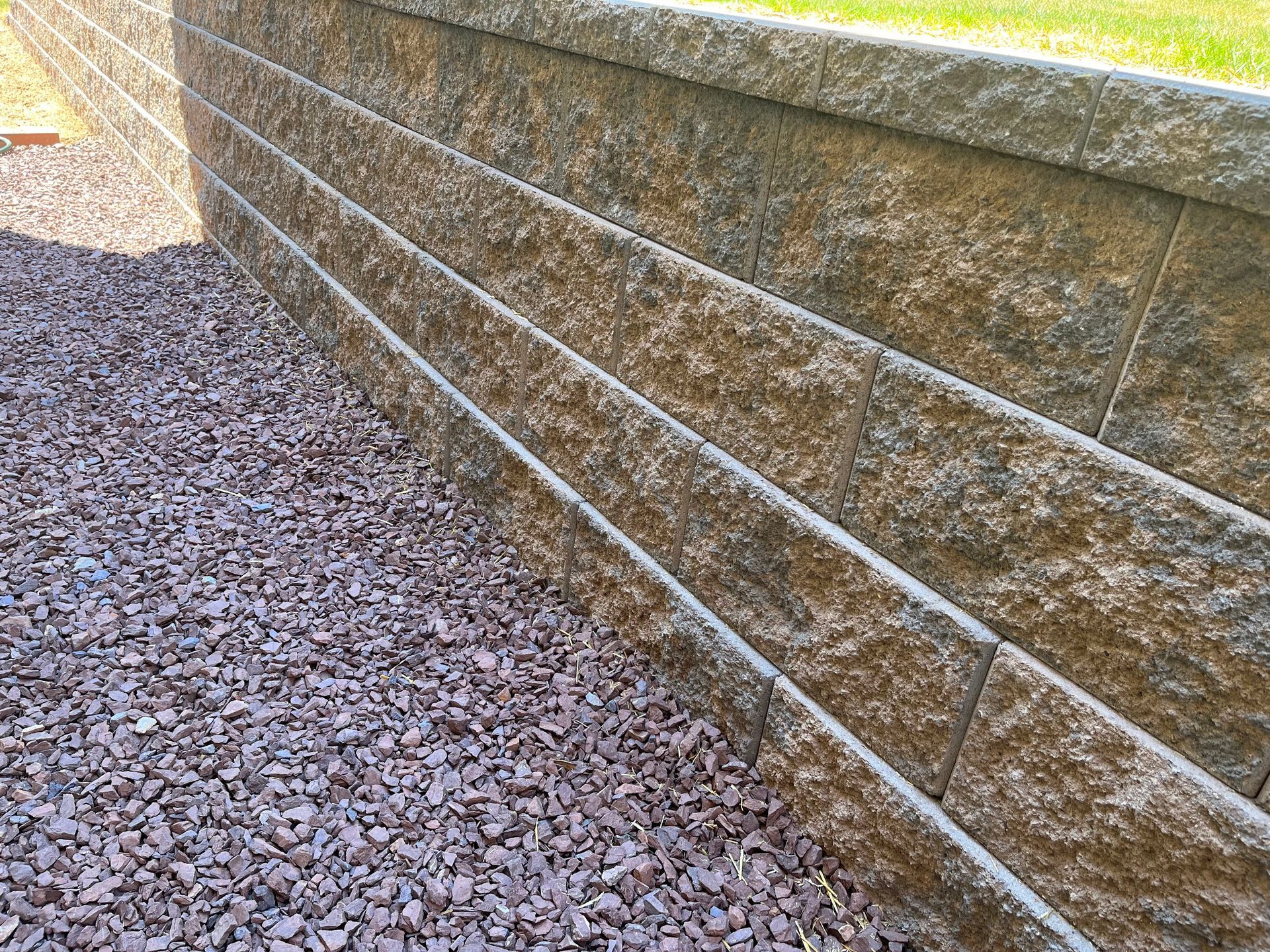 Stone retaining wall beside a gravel path, with horizontal white lines on tan blocks.